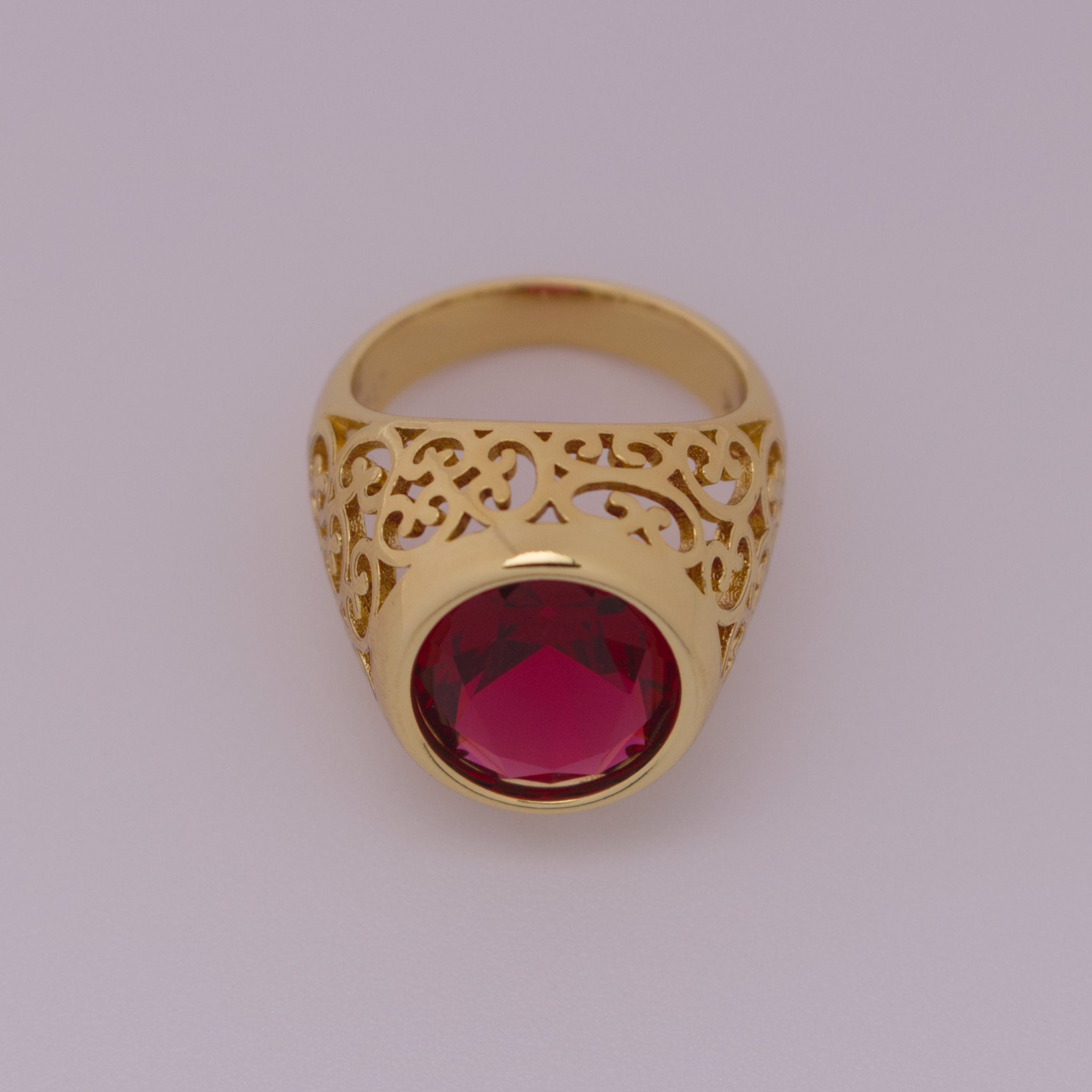 Gold ring with a red gemstone on a light gray background