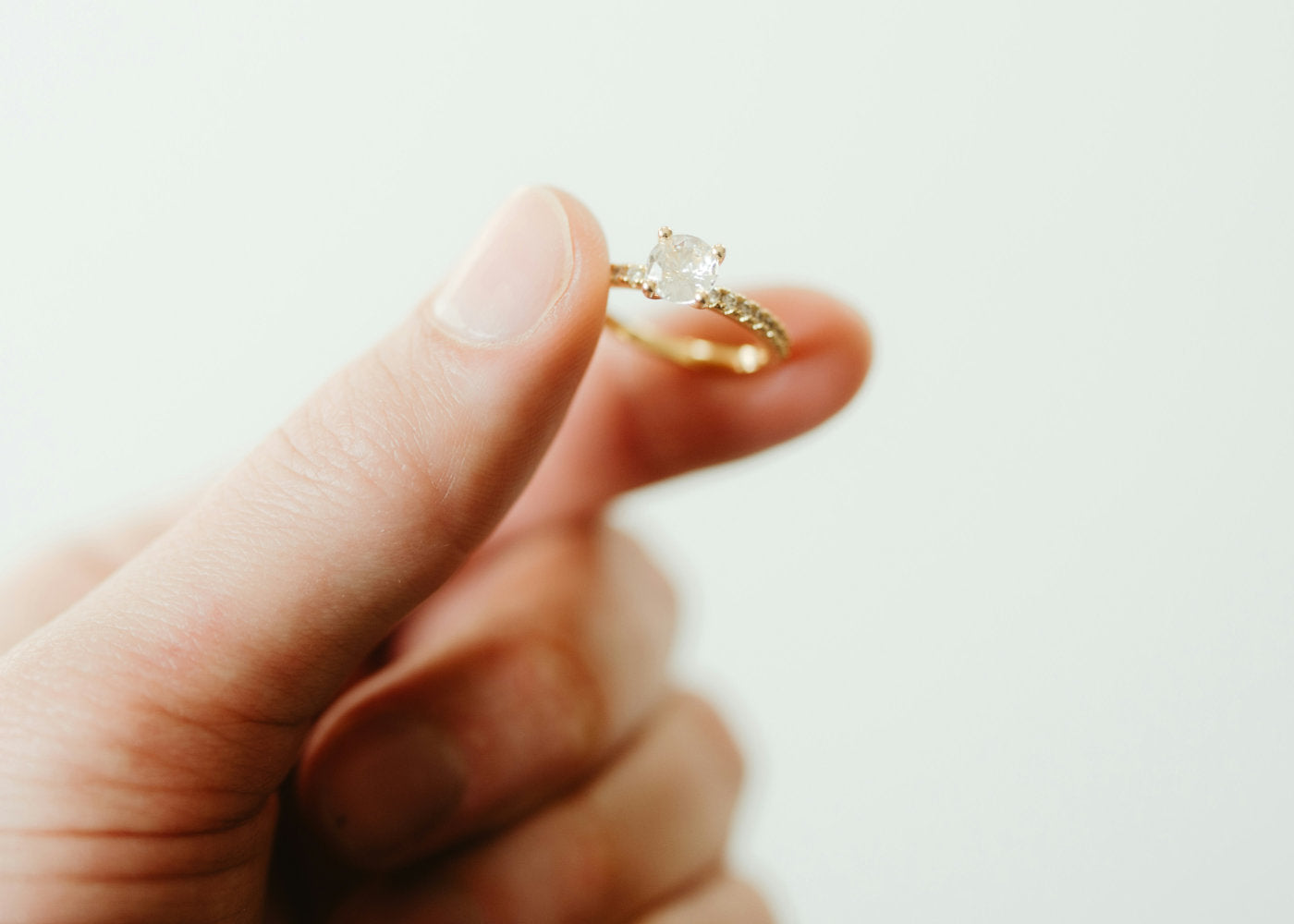 Gold ring with a diamond held between fingers against a light background