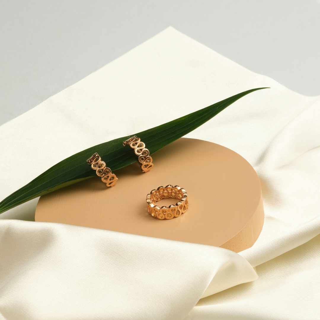 Gold earrings on a beige stone with a green leaf on a white fabric background