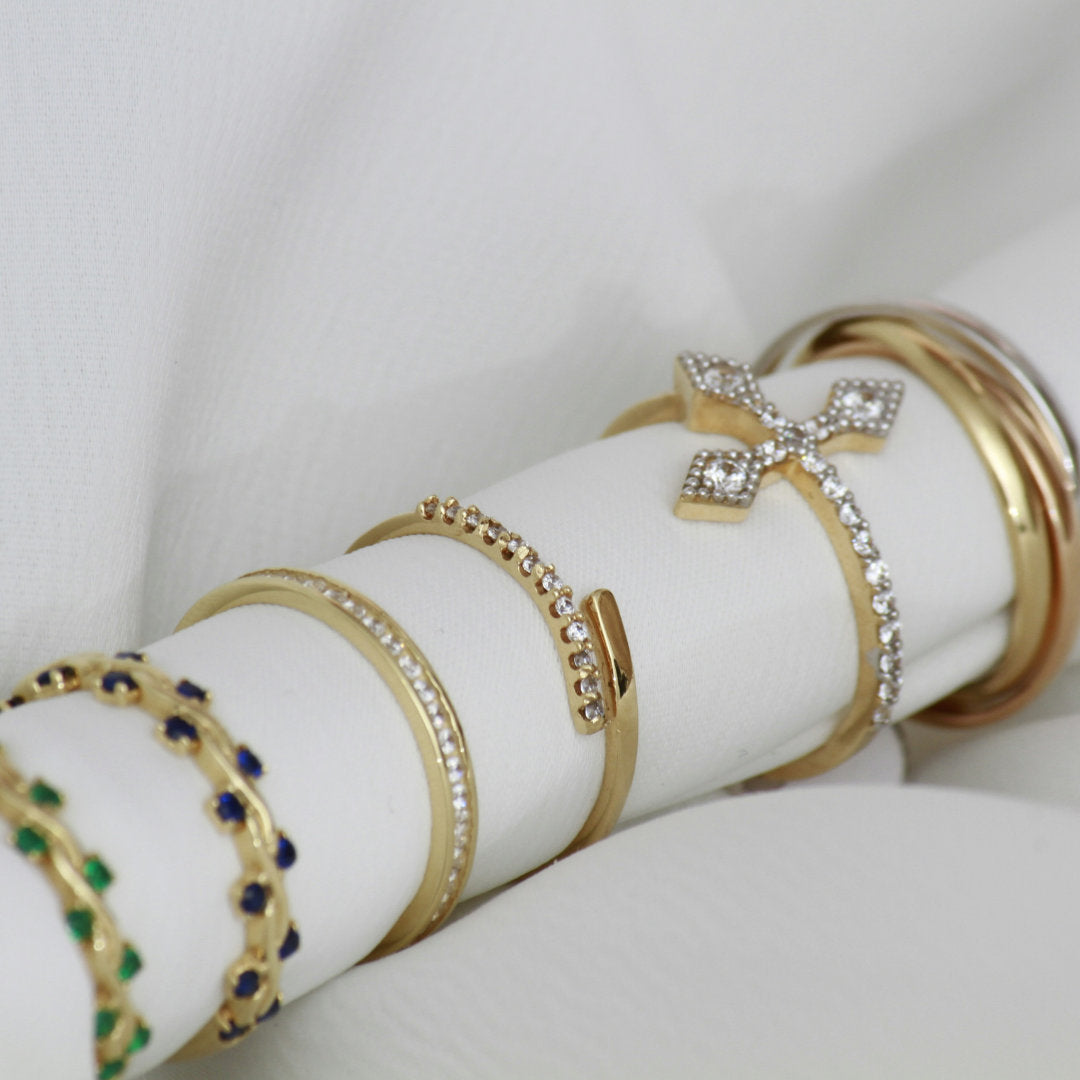 Gold bracelets with gemstones on a white cylindrical stand against a light gray background
