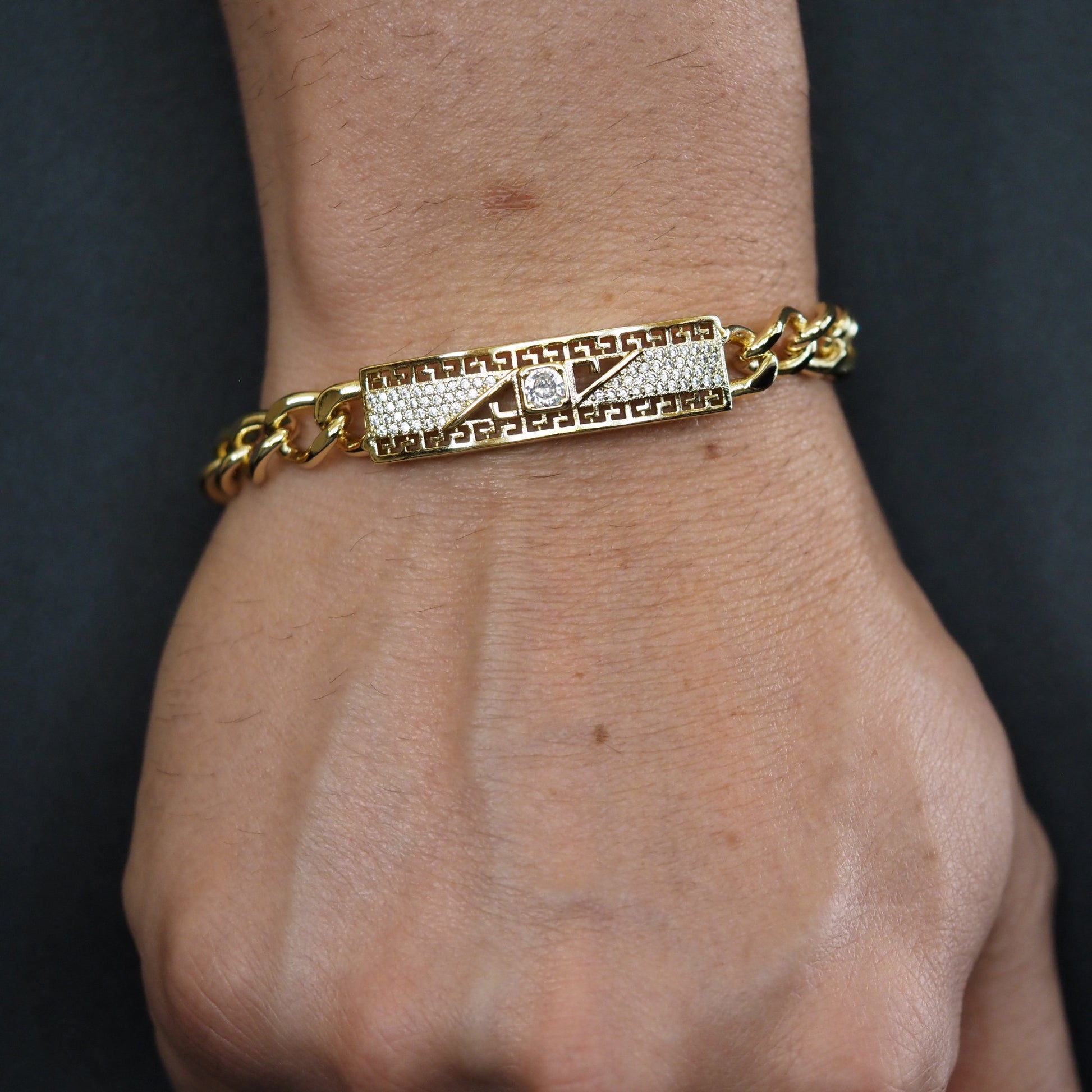 Gold bracelet with diamond accents on a wrist against a dark background