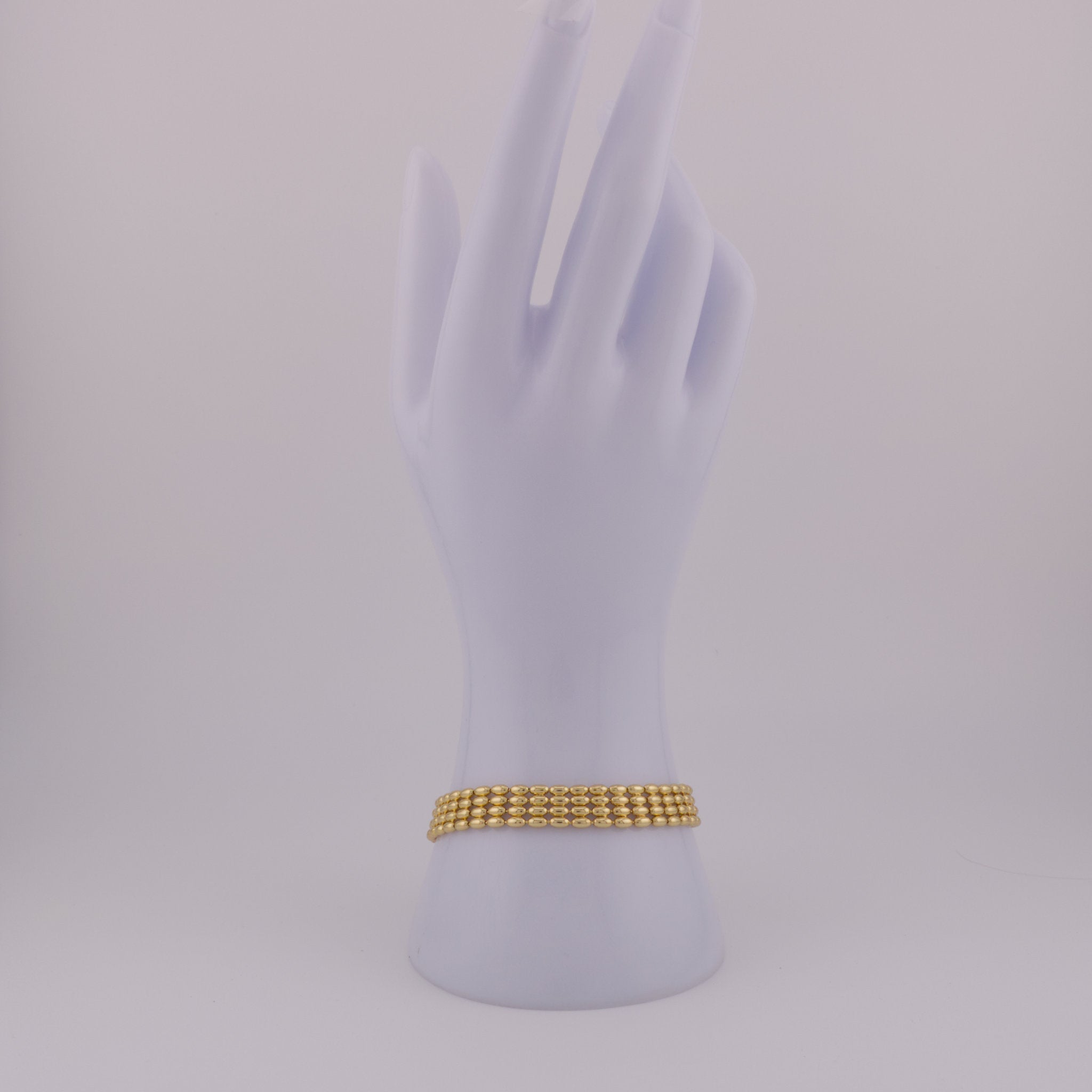 Gold bracelet on a mannequin hand against a light gray background