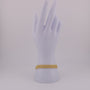 Gold bracelet on a mannequin hand against a light gray background