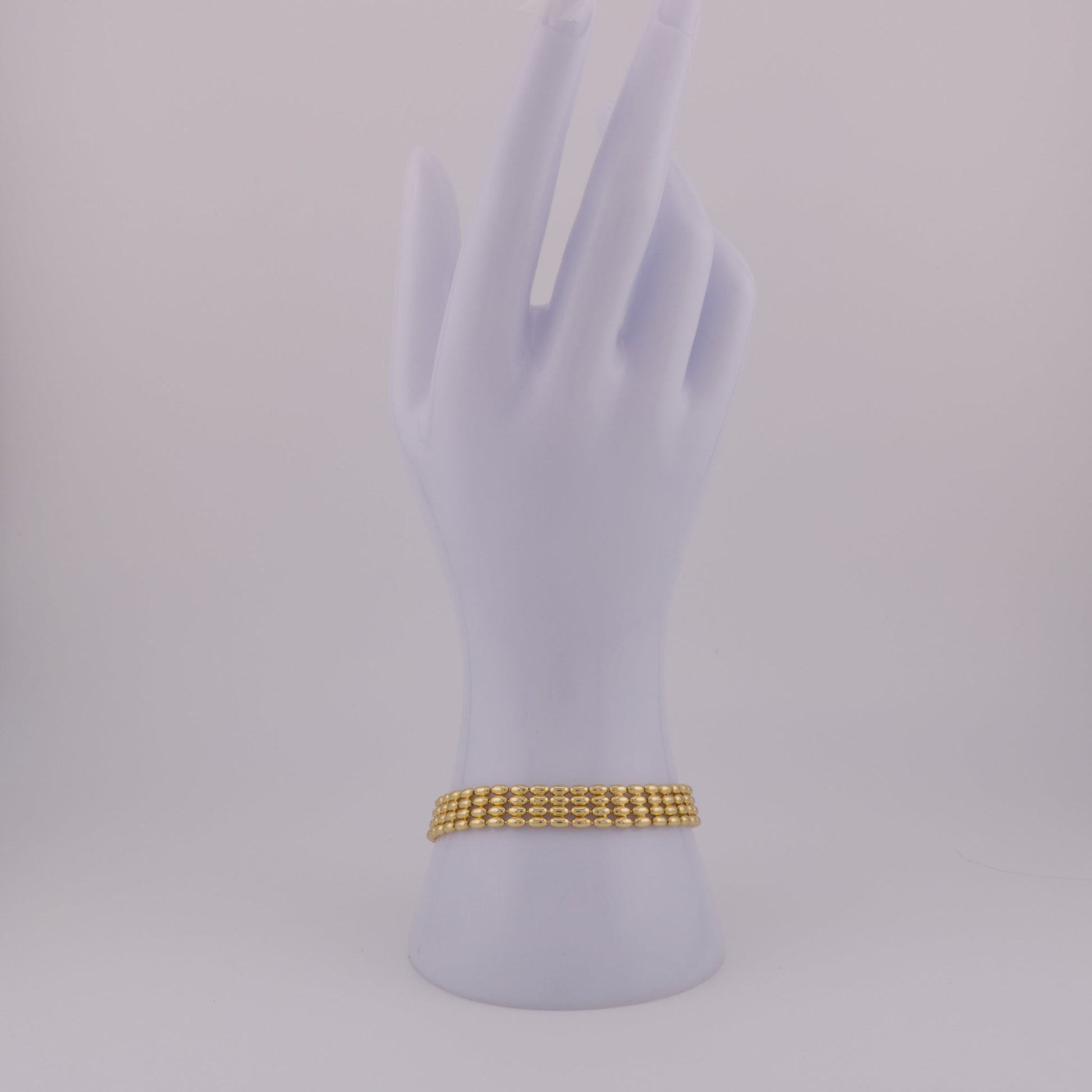 Gold bracelet on a mannequin hand against a light gray background