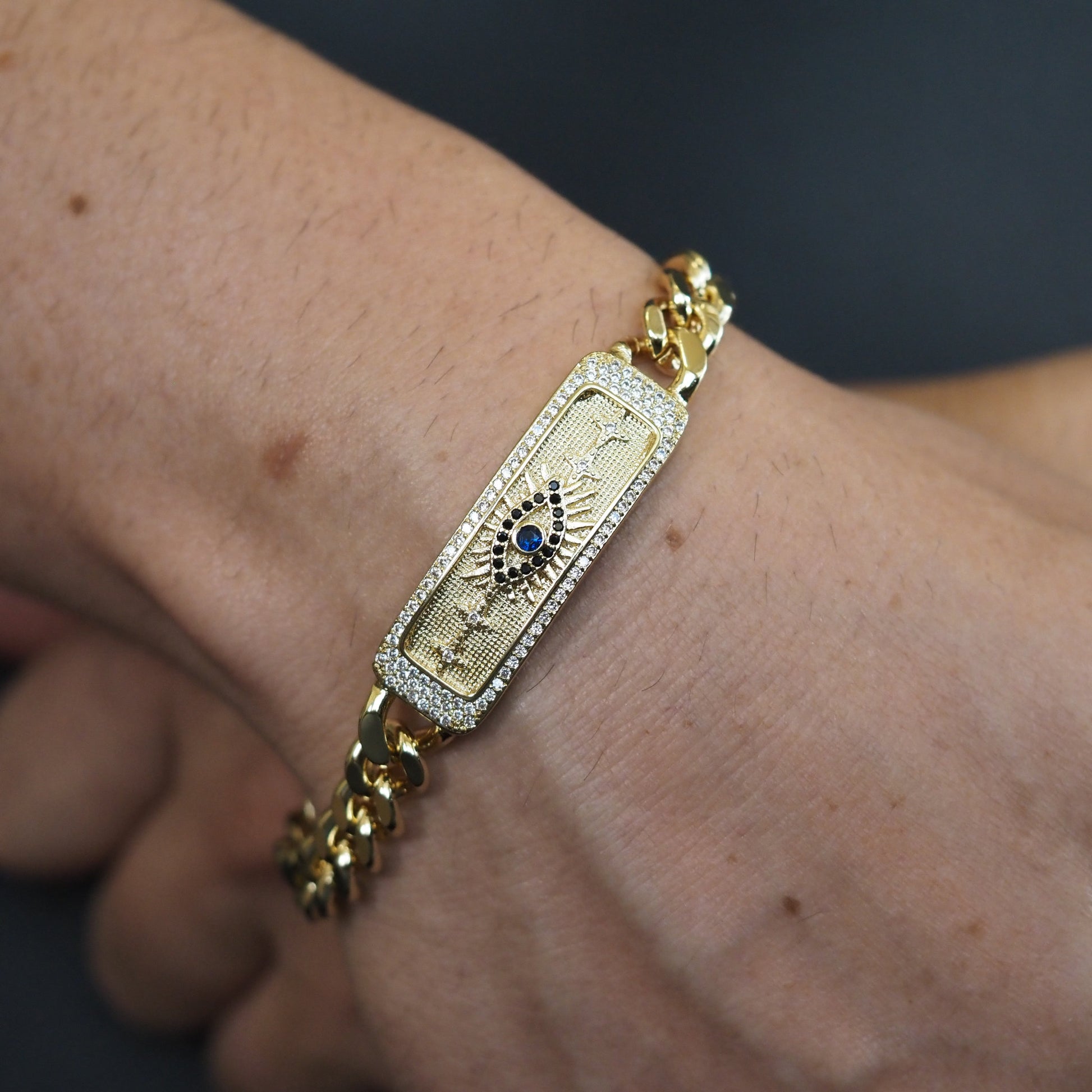 Gold bracelet with a decorative clasp on a wrist against a dark background