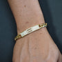 Gold bracelet with engraved text on a wrist against a dark background