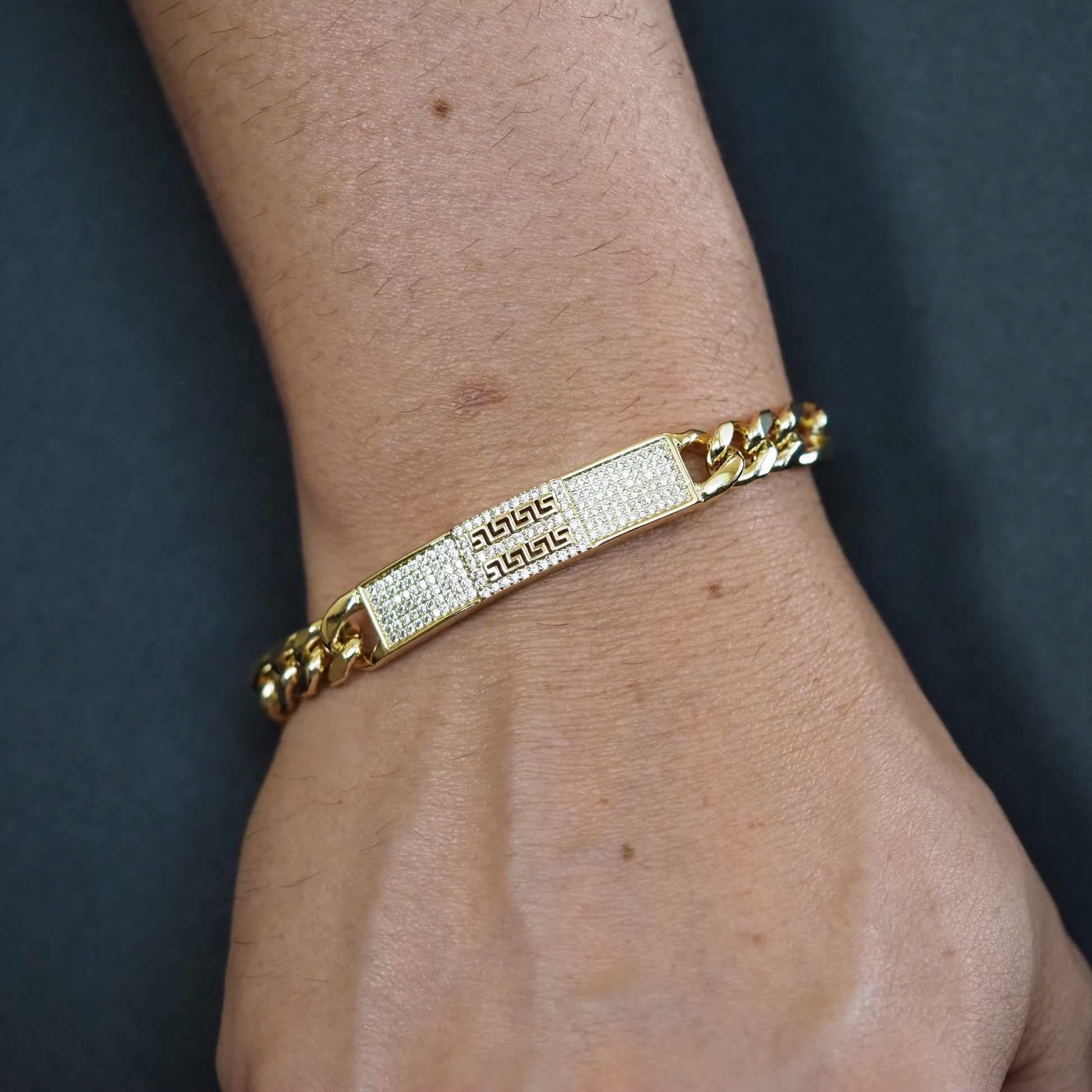 Gold bracelet with engraved text on a wrist against a dark background