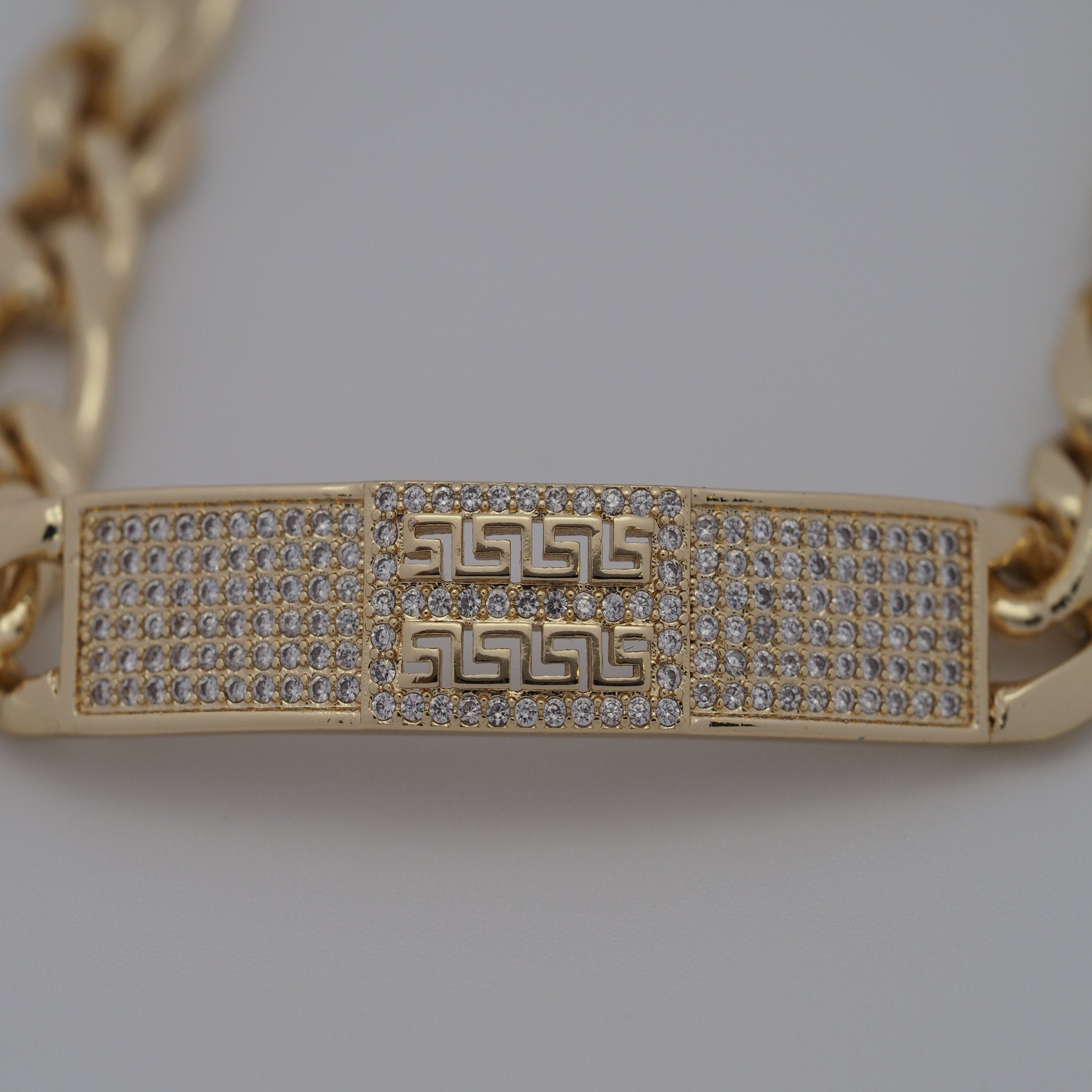 Gold bracelet with intricate design and gemstones on a light gray background