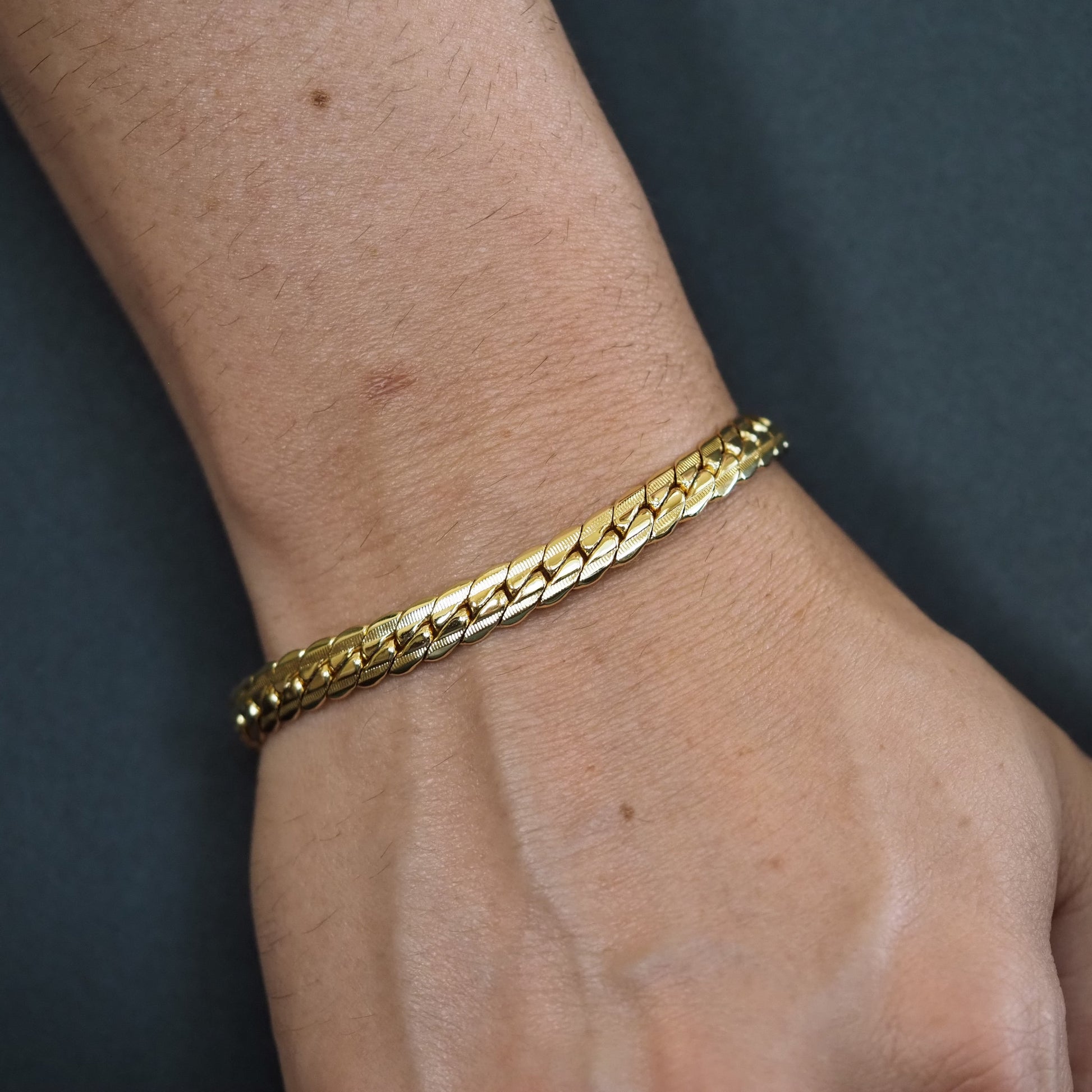 Gold bracelet on a wrist against a dark background