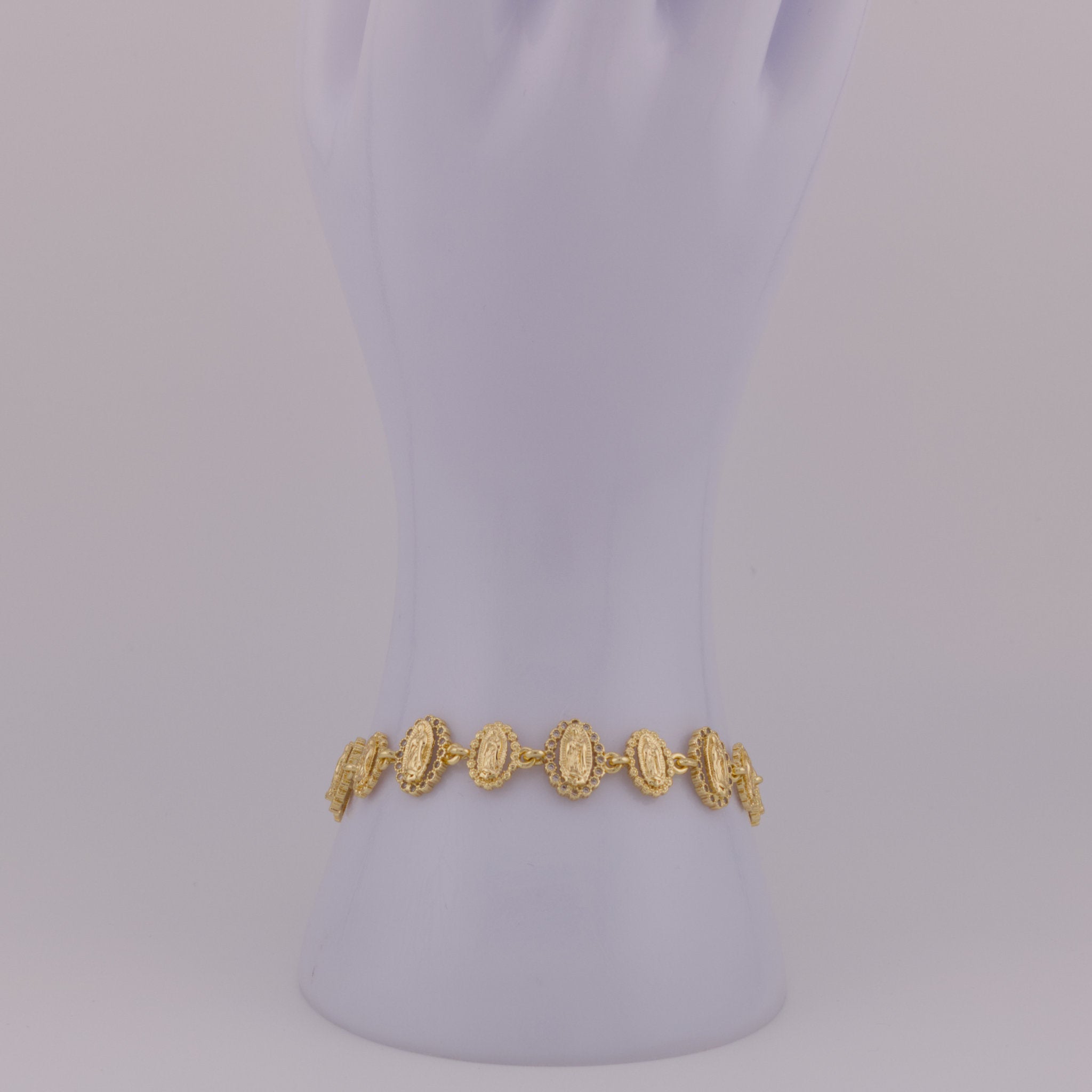 Gold bracelet on a mannequin arm against a light purple background