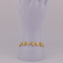 Gold bracelet on a mannequin arm against a light purple background