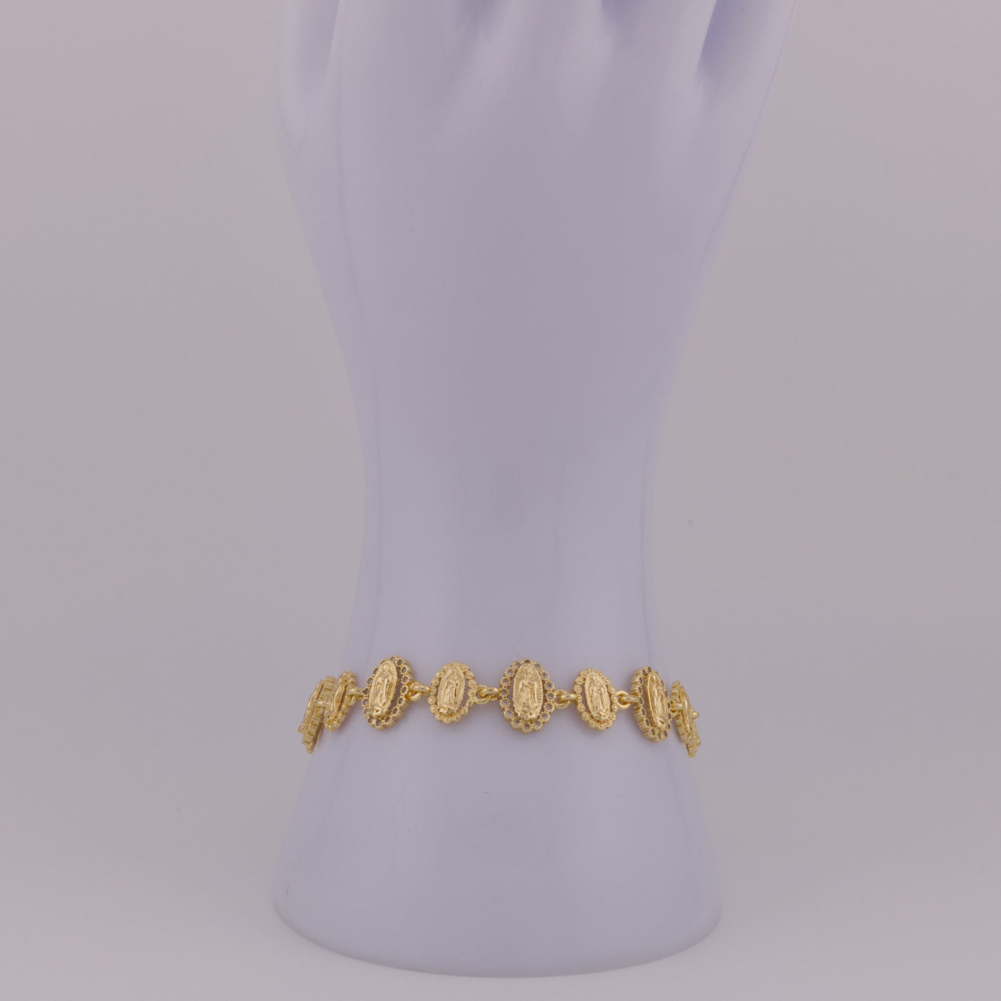 Gold bracelet on a mannequin arm against a light purple background