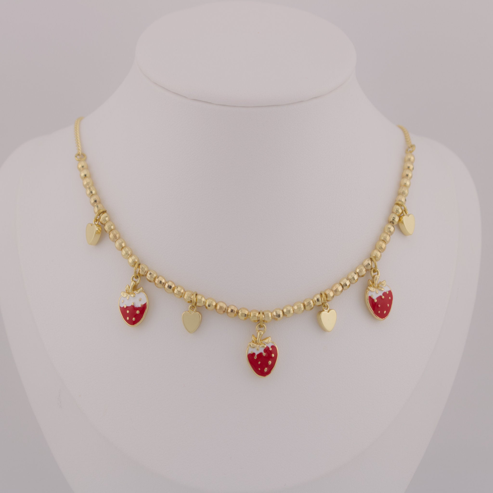 Gold necklace with strawberry-shaped charms on a mannequin bust.
