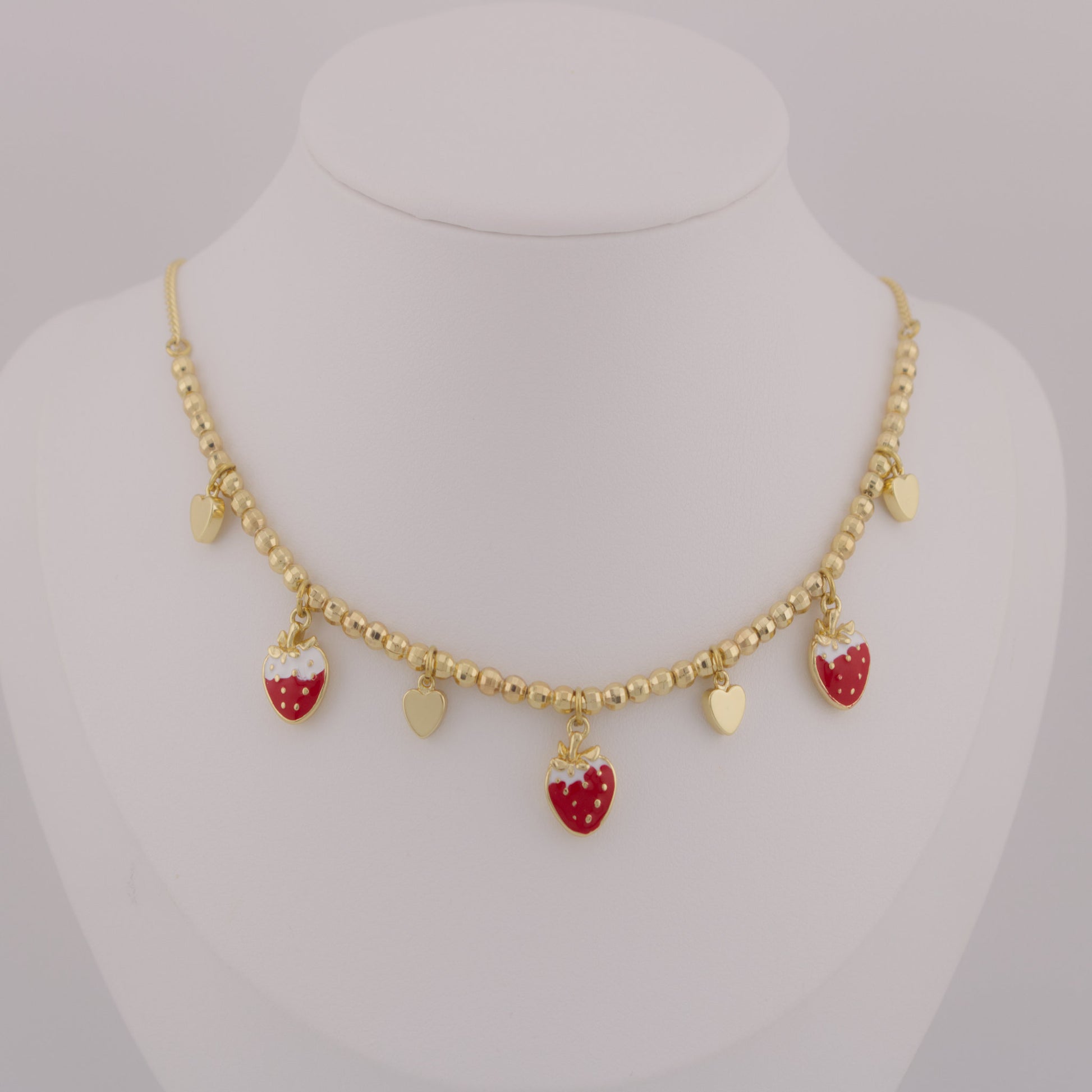 Gold necklace with strawberry-shaped charms on a mannequin bust.