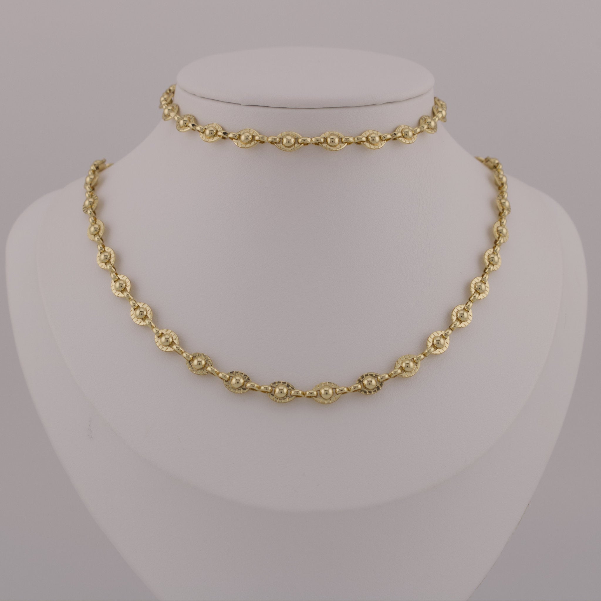 Gold necklace on a mannequin bust against a gray background