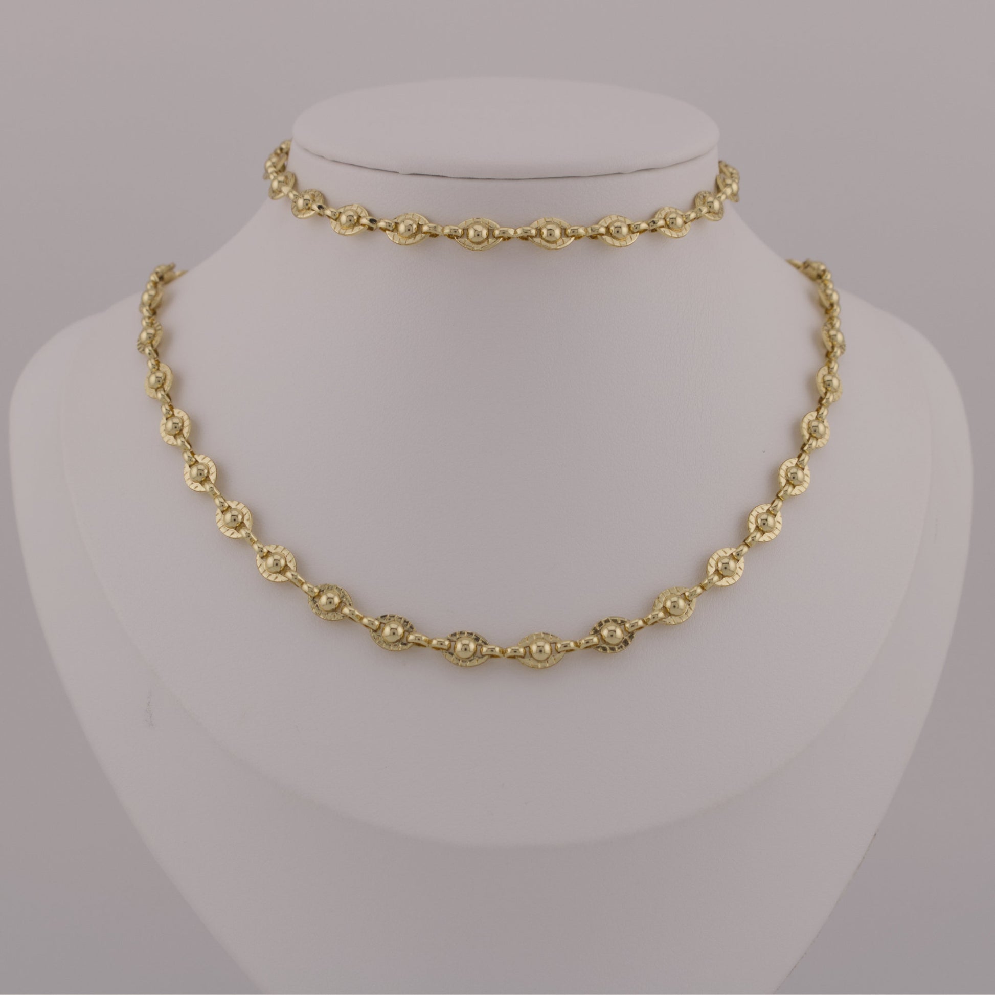 Gold necklace on a mannequin bust against a gray background