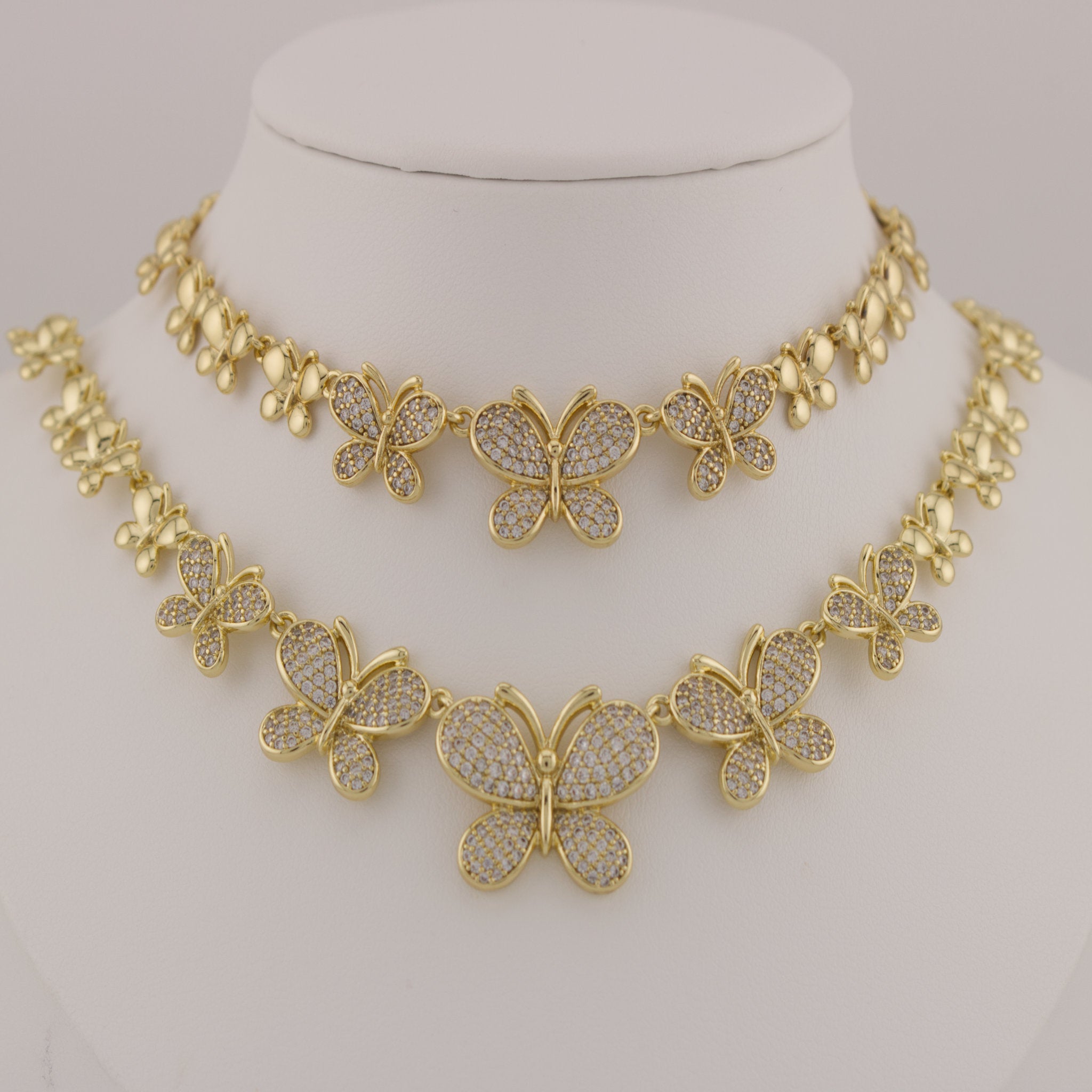 Gold butterfly necklace on a mannequin bust against a neutral background