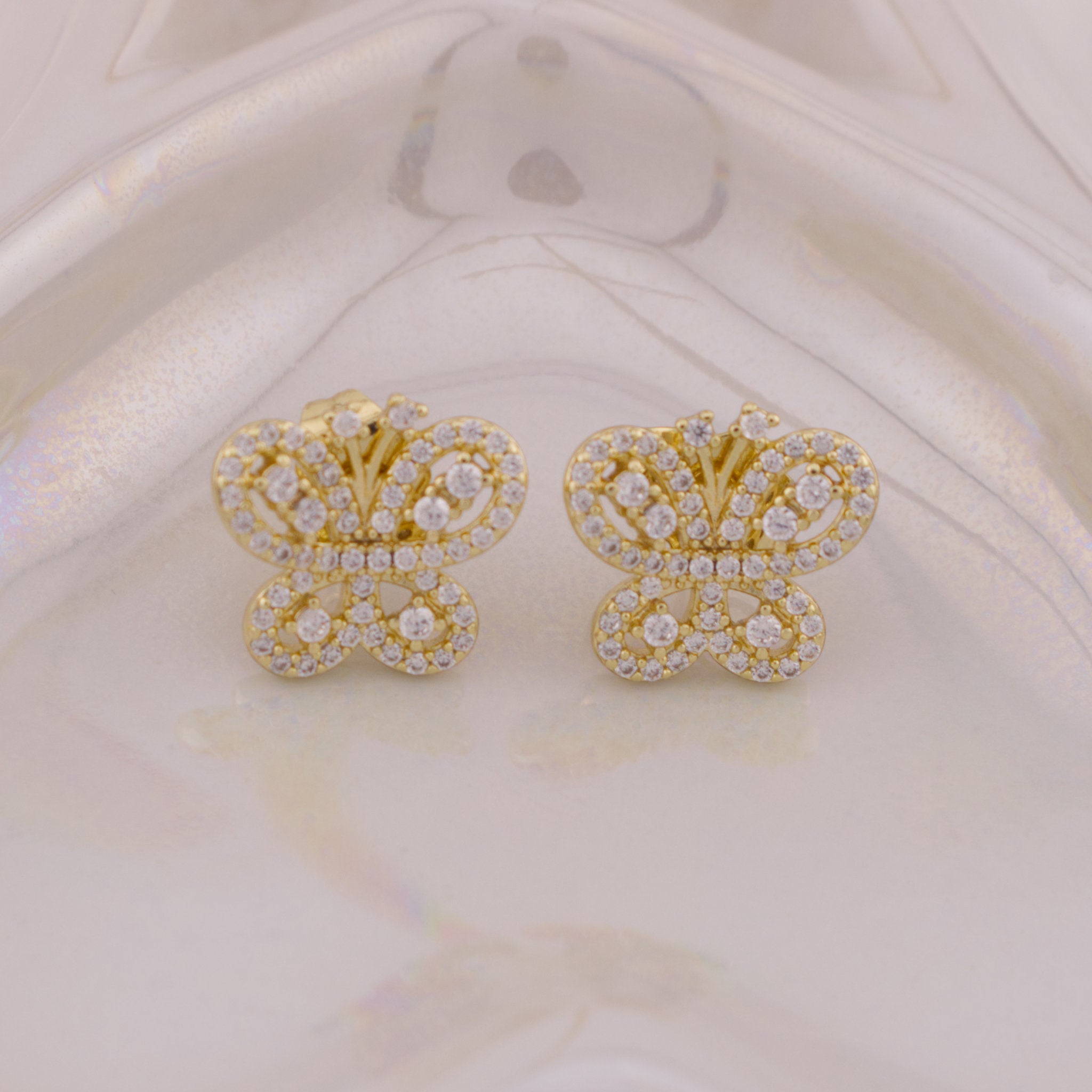 Gold butterfly earrings with clear stones on a beige background