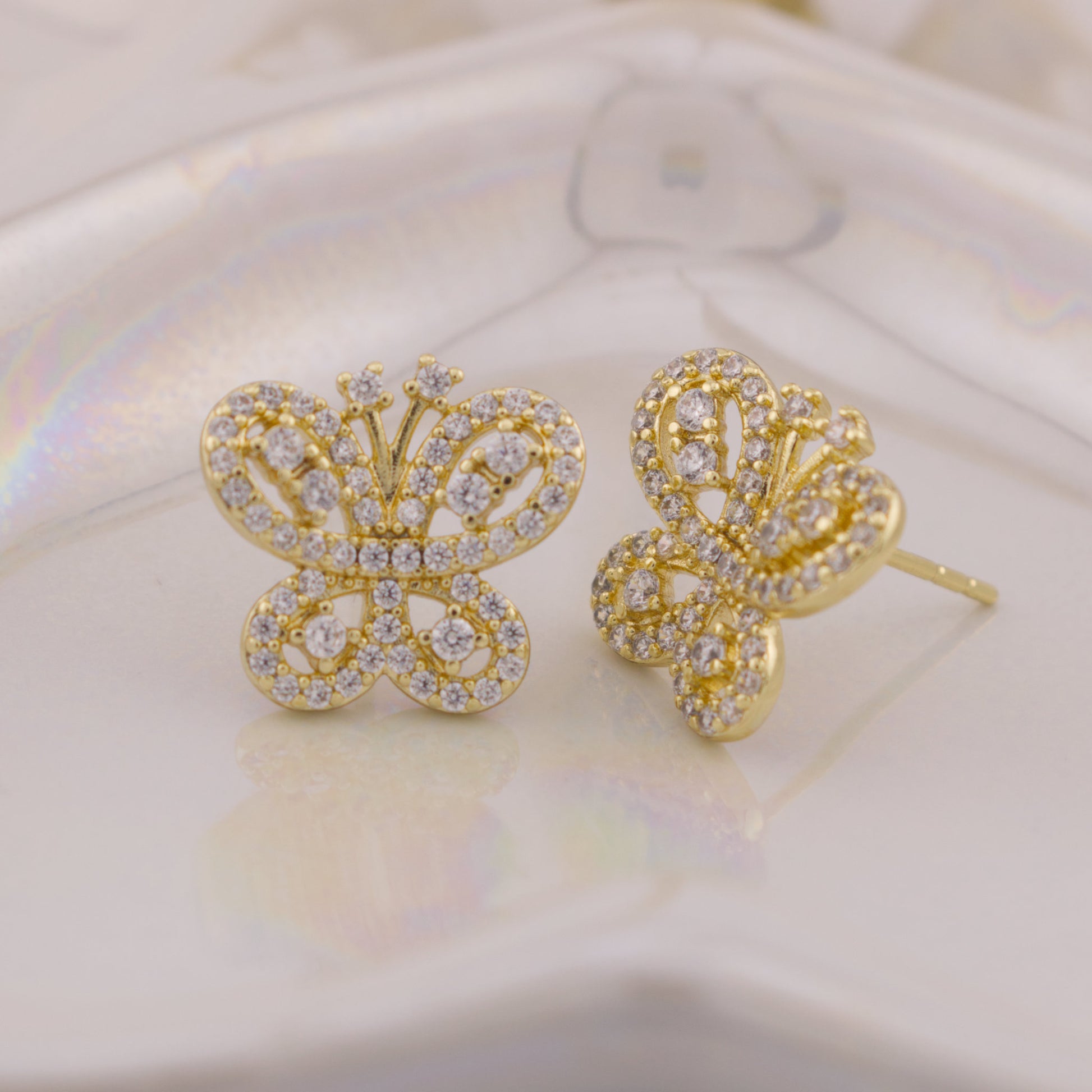 Gold butterfly earrings with gemstones on a soft white background