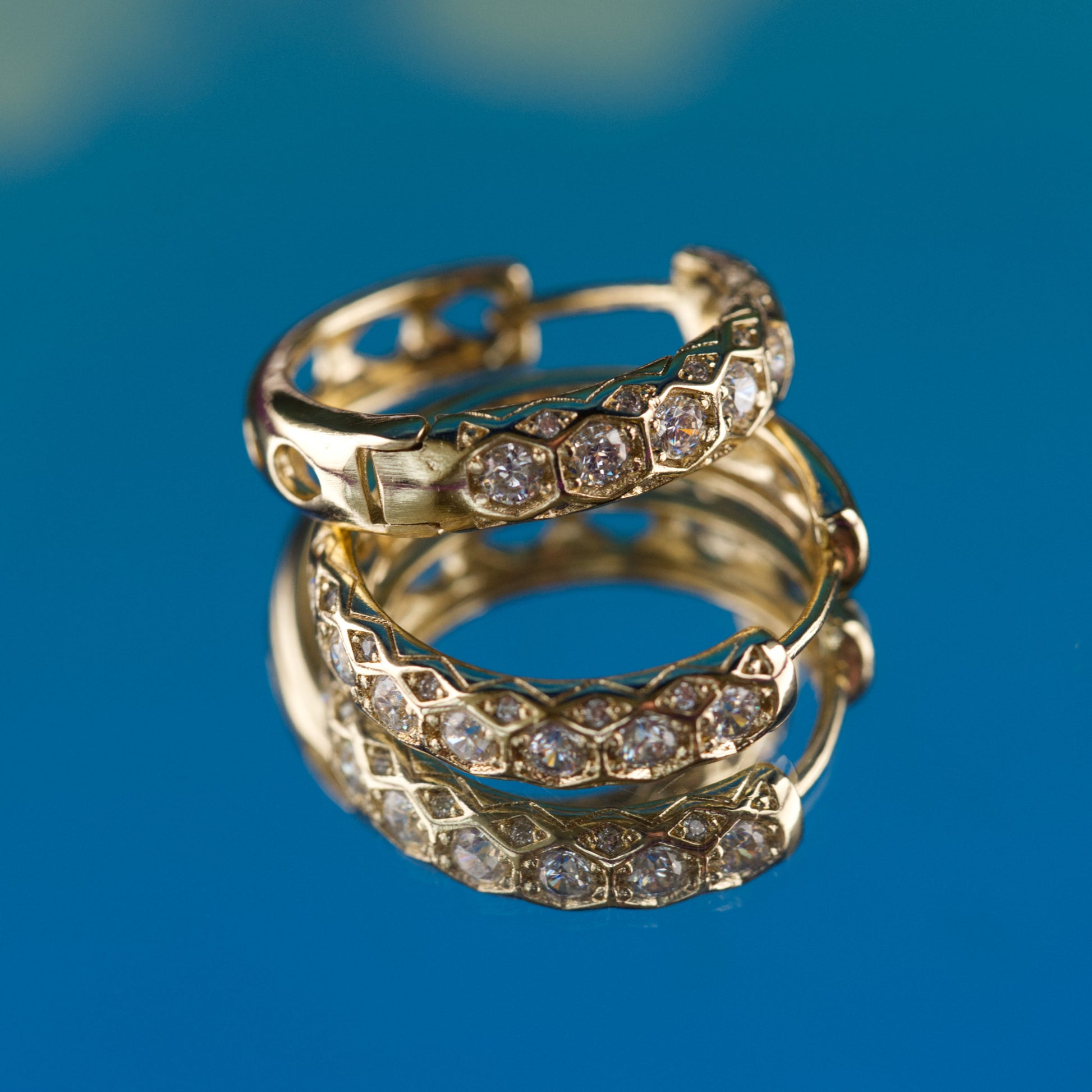 Gold hoop earrings with diamond accents on a blue background