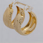 Gold hoop earrings with intricate designs on a light gray background