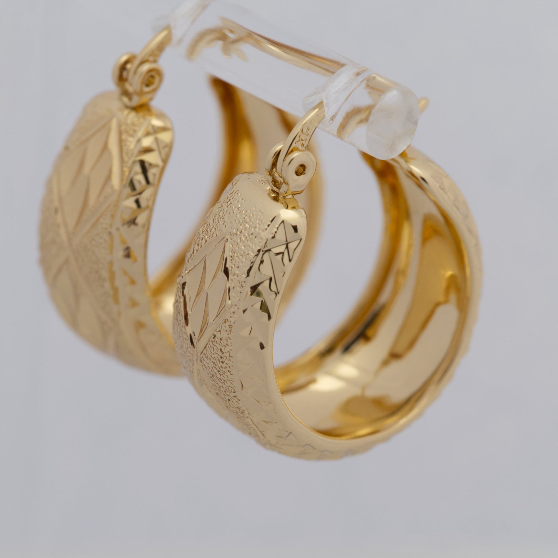 Gold hoop earrings with intricate designs on a light gray background