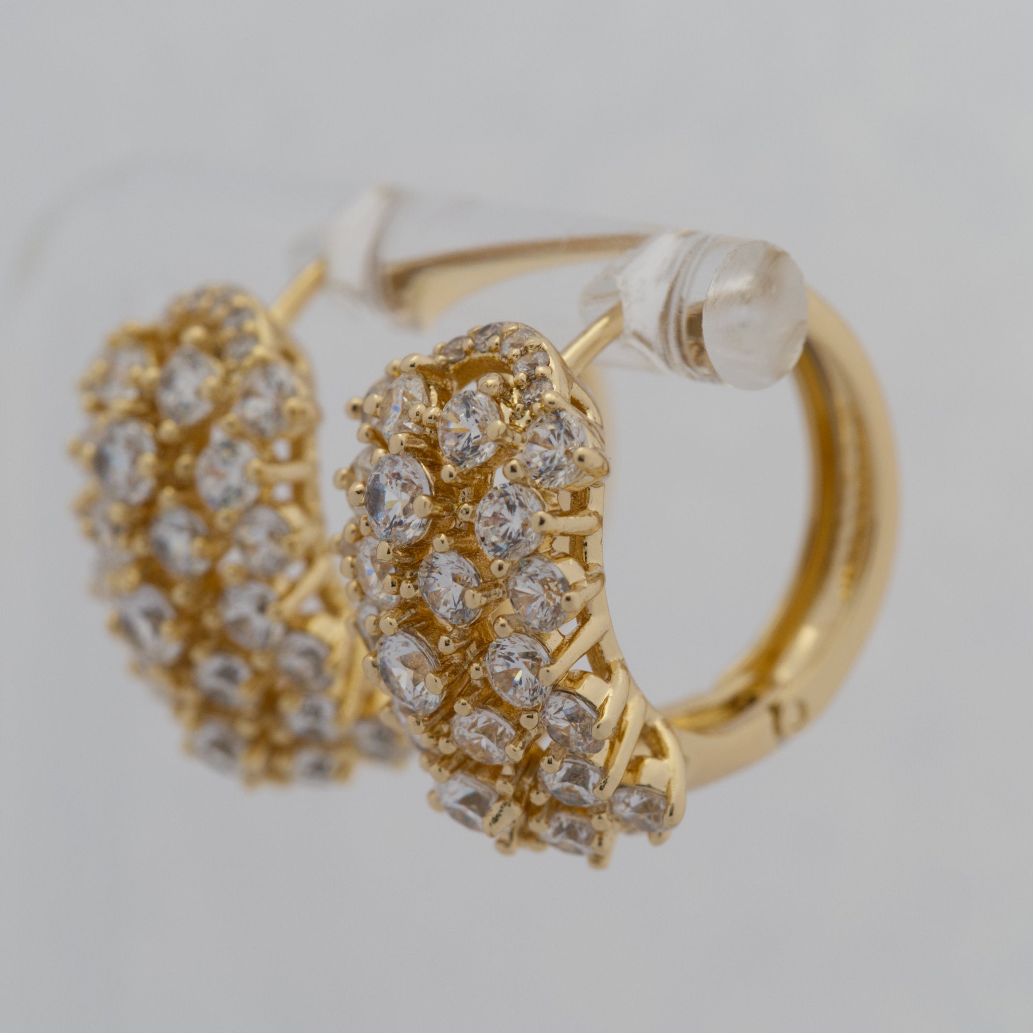 Gold hoop earrings with diamond-like stones on a light gray background