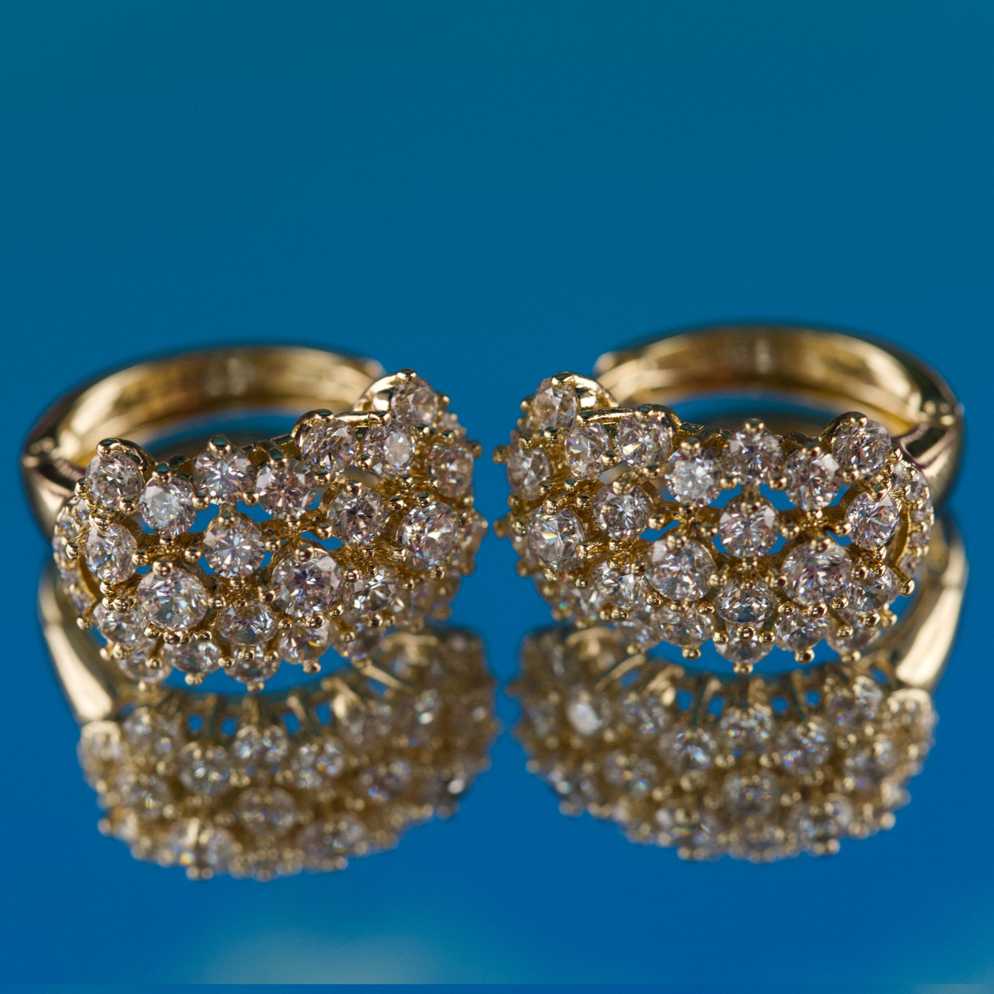 Pair of gold earrings with diamond-like stones on a blue background