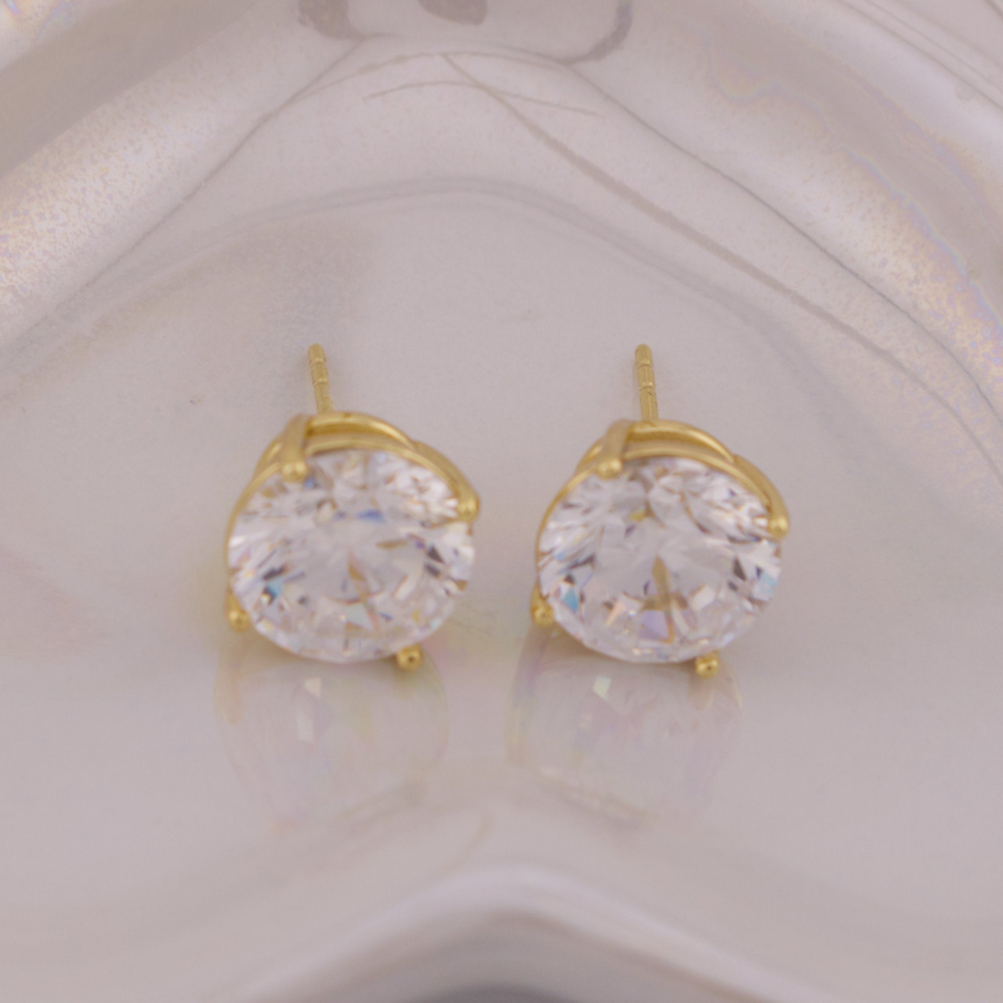 Gold earrings with large clear gemstones on a light background
