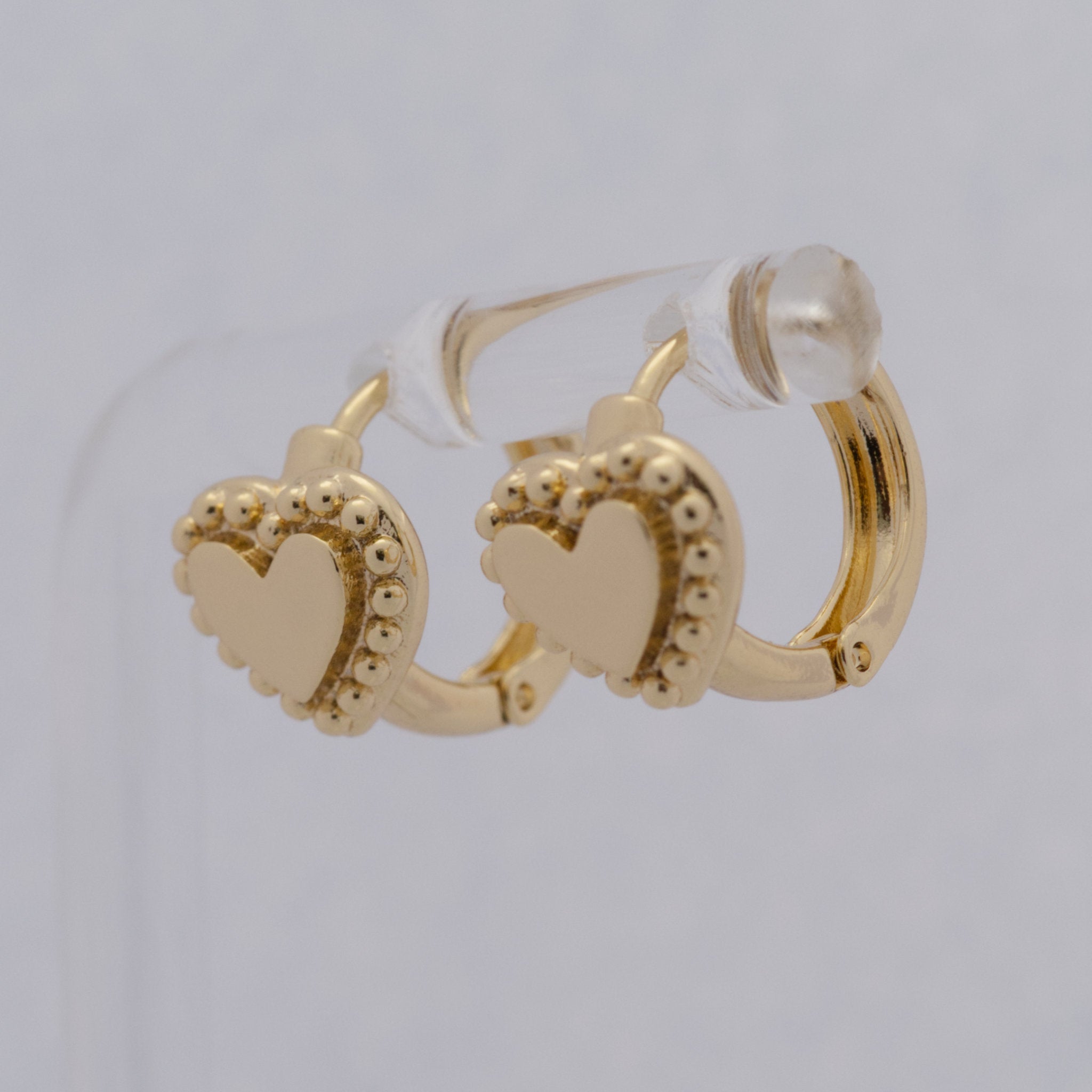 Gold hoop earrings with heart designs on a light gray background