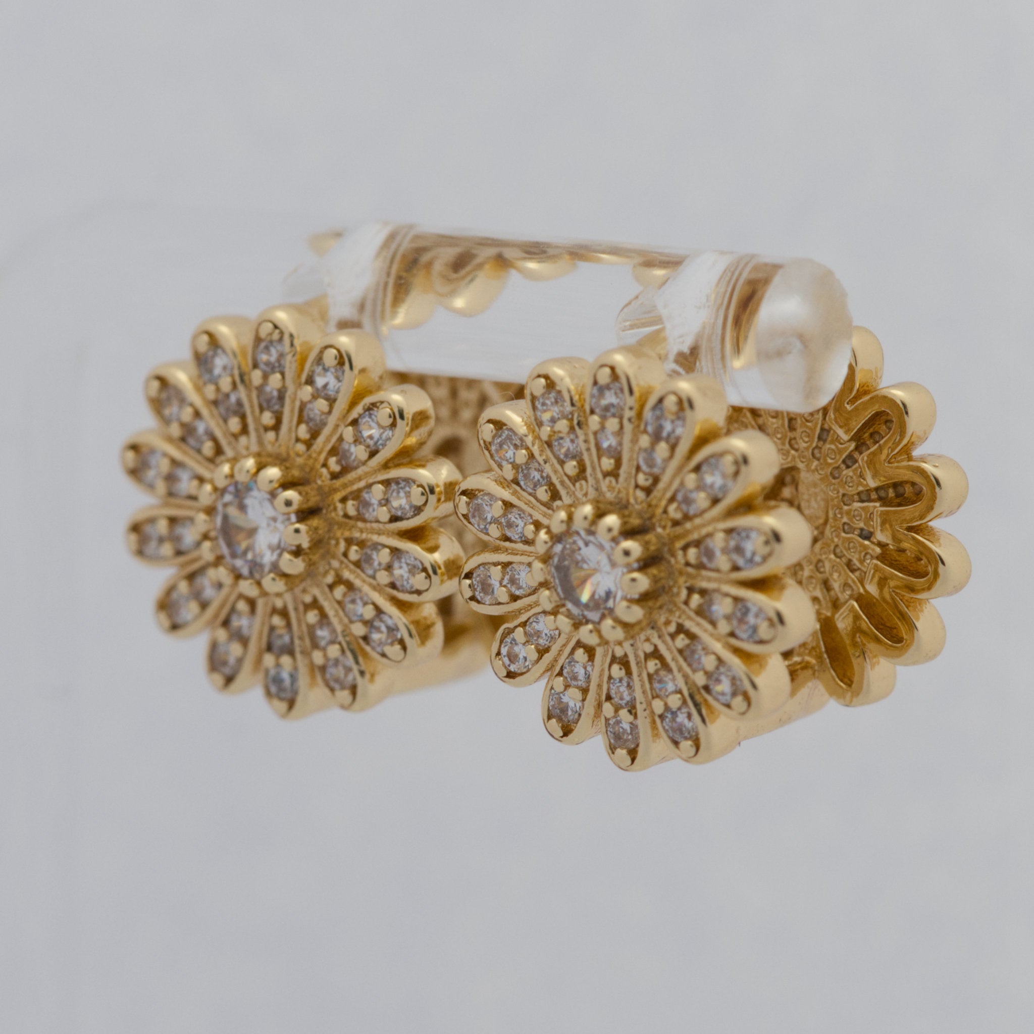 Gold hoop earrings with floral design and clear gemstones on a light gray background