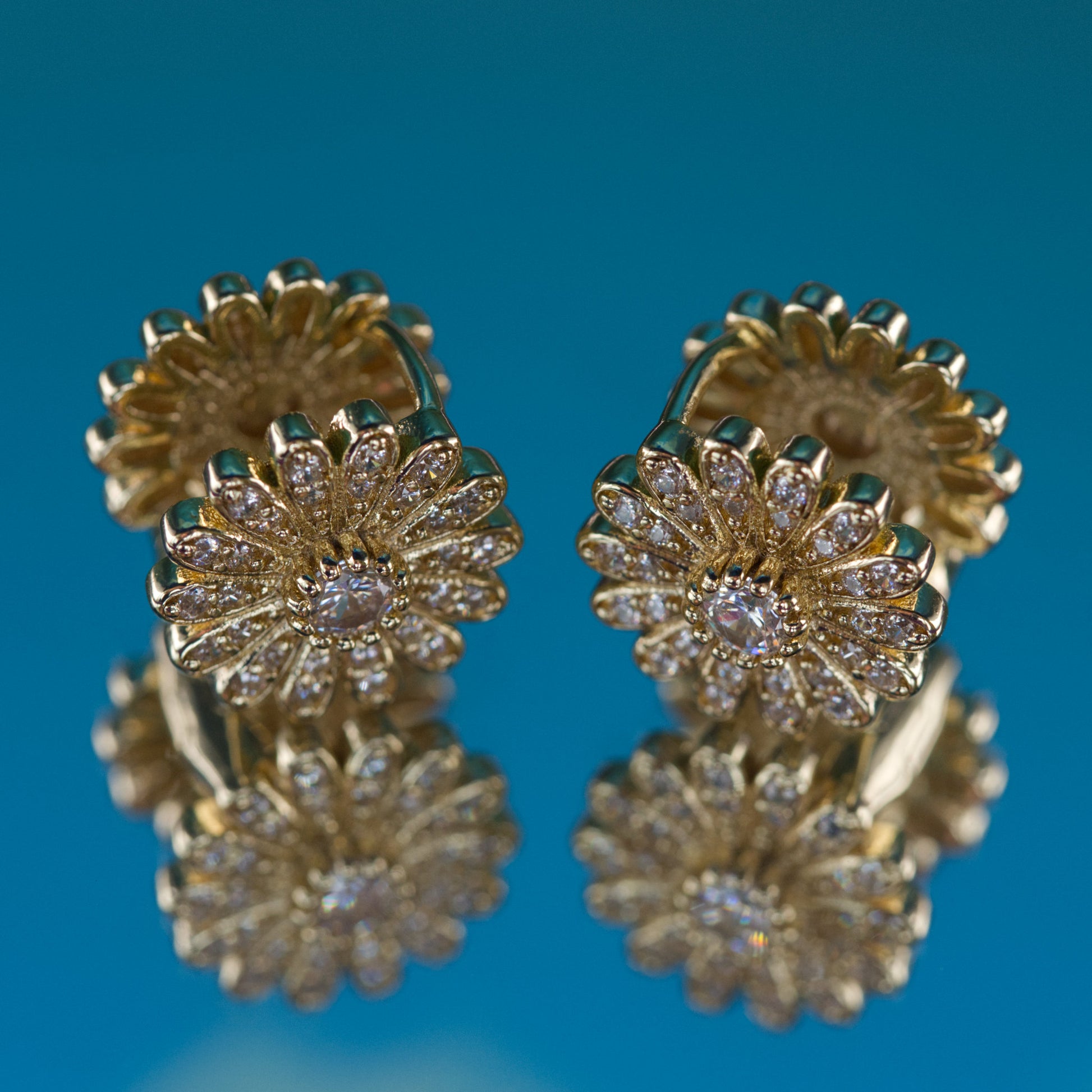 Gold earrings with diamond-like stones on a blue background
