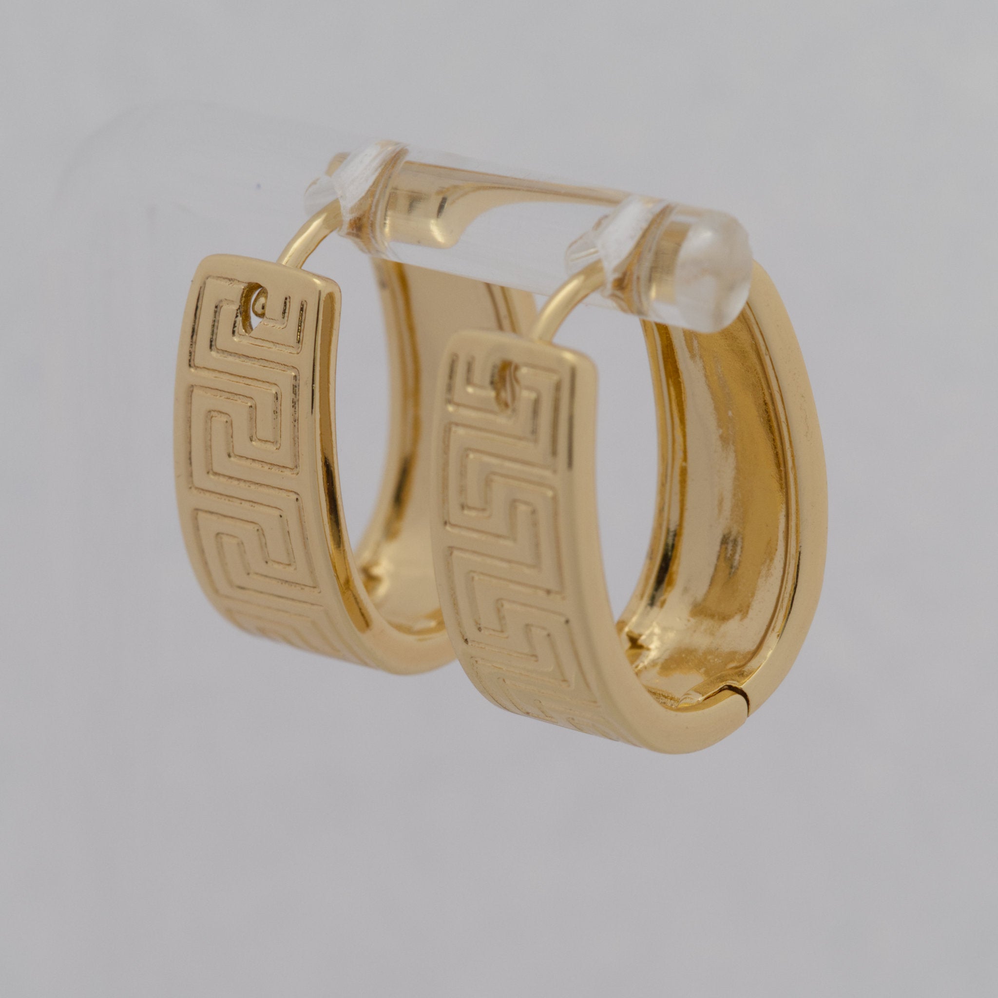 Gold hoop earrings with a geometric pattern on a light gray background