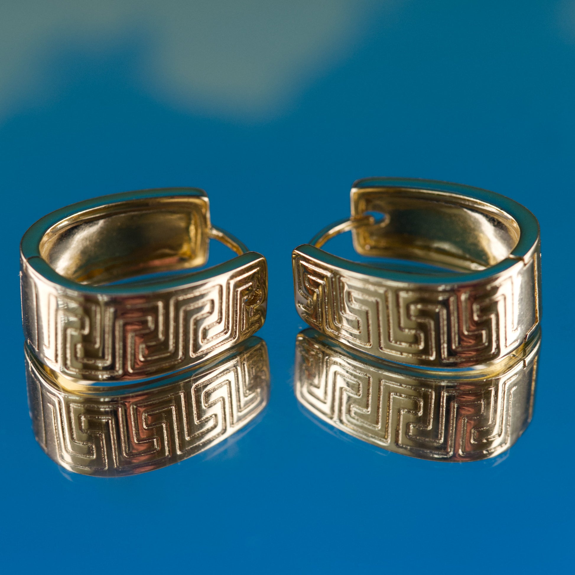 Pair of gold hoop earrings with intricate design on a blue background