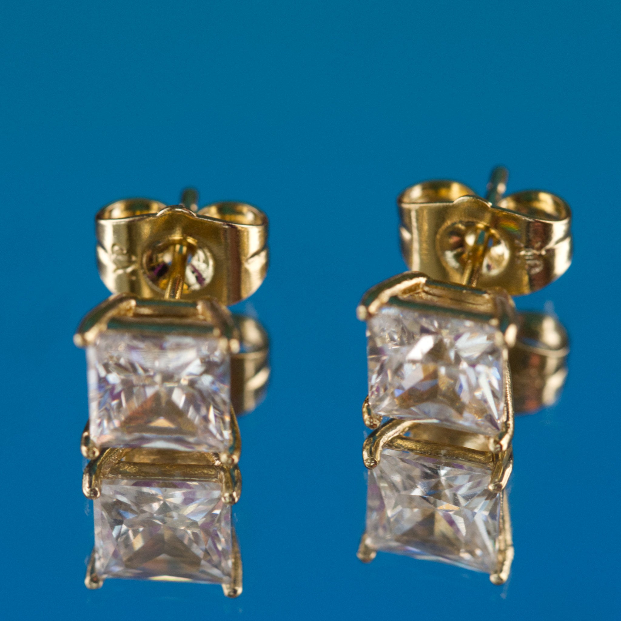 Gold earrings with square-cut gemstones on a blue background
