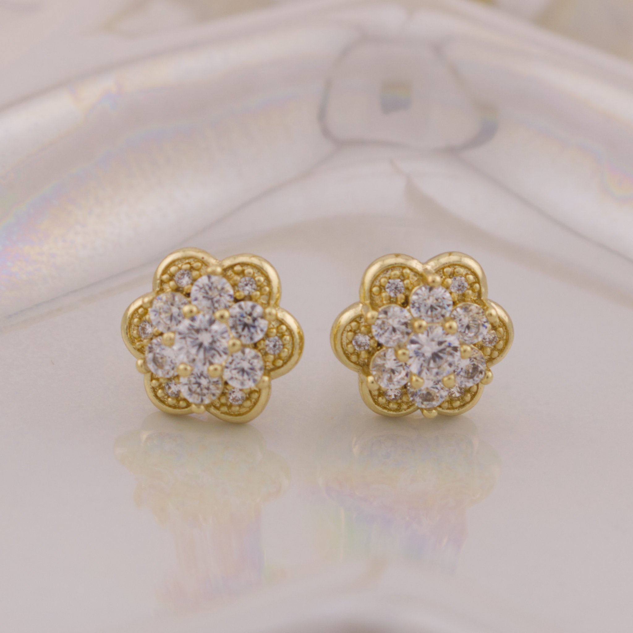 Gold flower-shaped earrings with clear gemstones on a light background