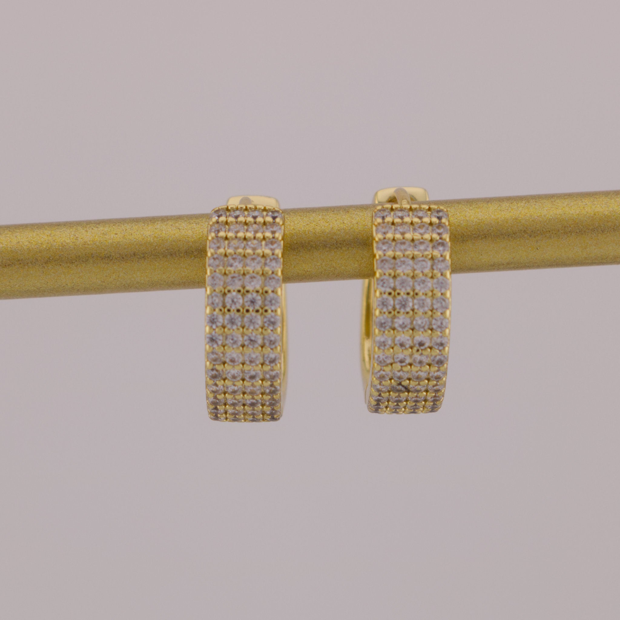 Gold hoop earrings with clear stones on a gold rod against a gray background