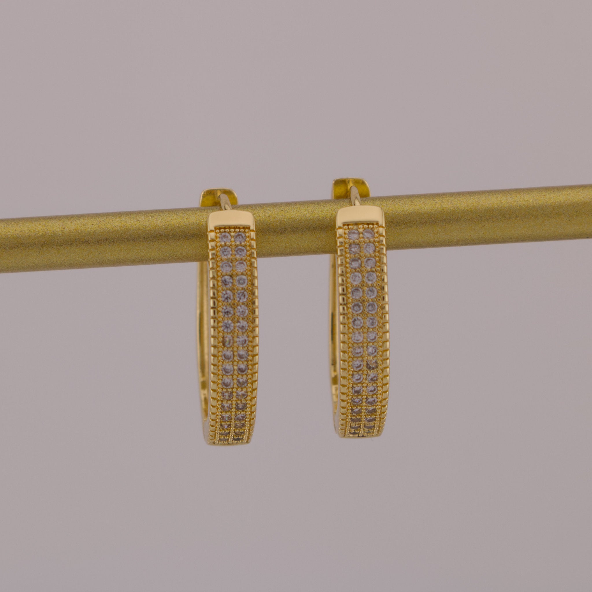 Gold hoop earrings with embedded stones on a gray background