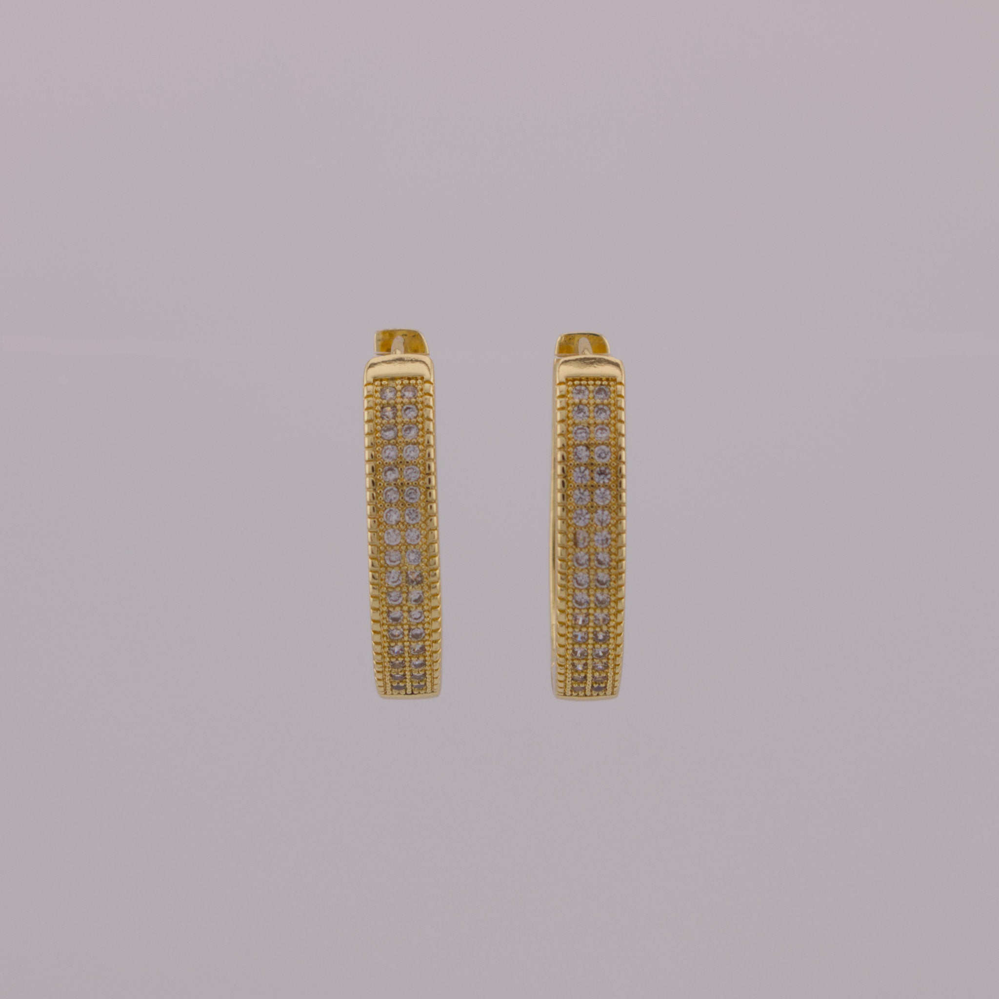 Gold hoop earrings with embedded stones on a gray background