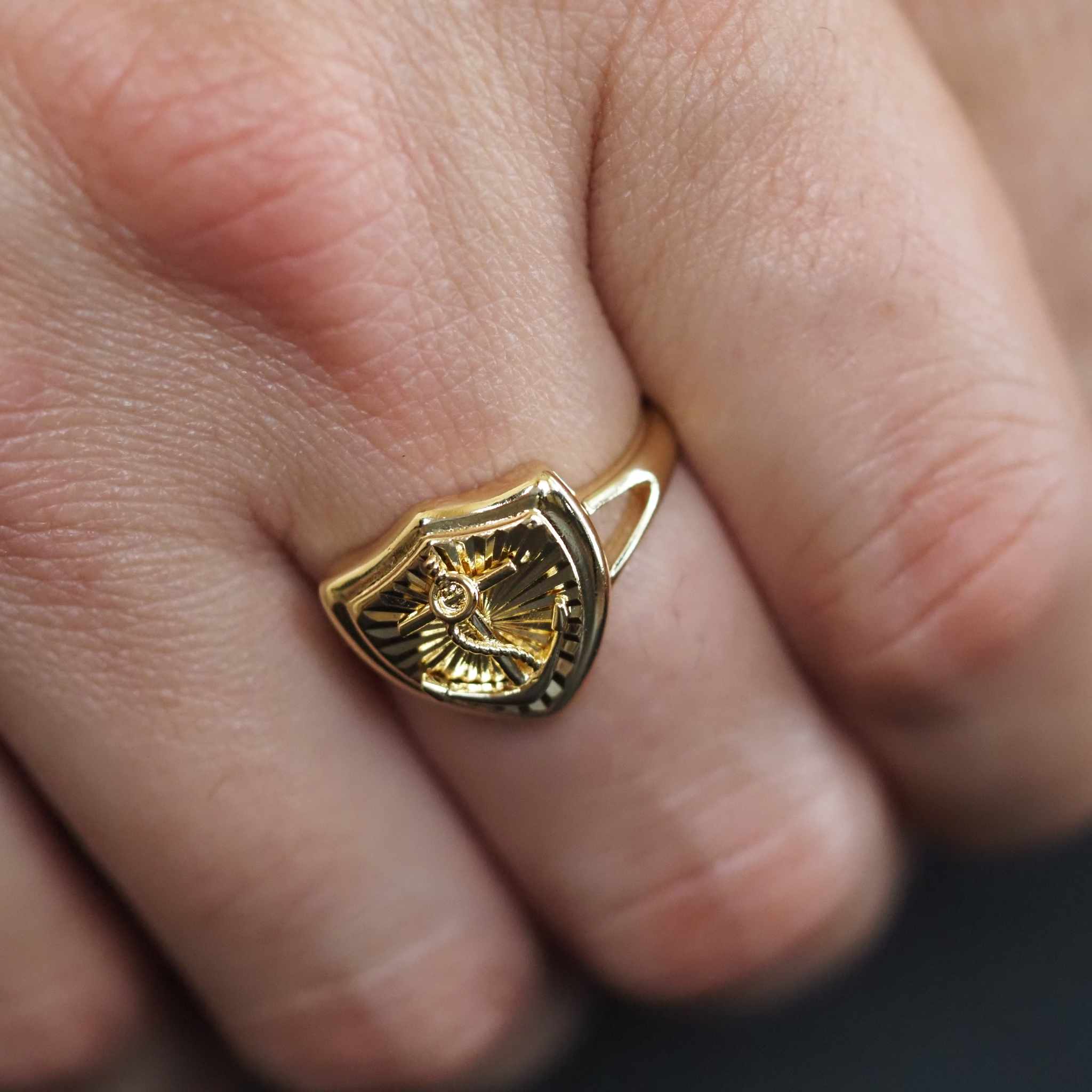 Gold ring with a shield design on a finger