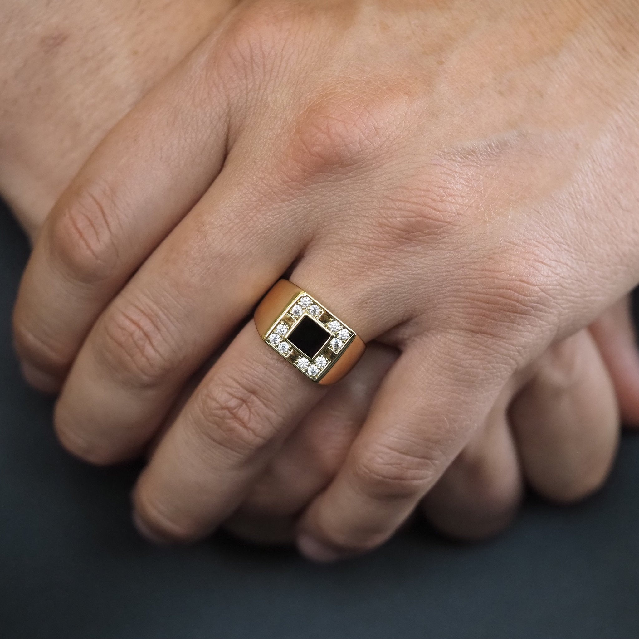 Close-up of a hand wearing a gold ring with a black center stone on a dark background