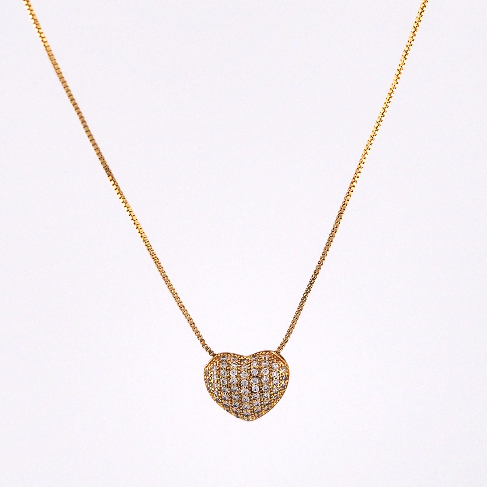 Heart-shaped diamond pendant on a gold chain against a white background