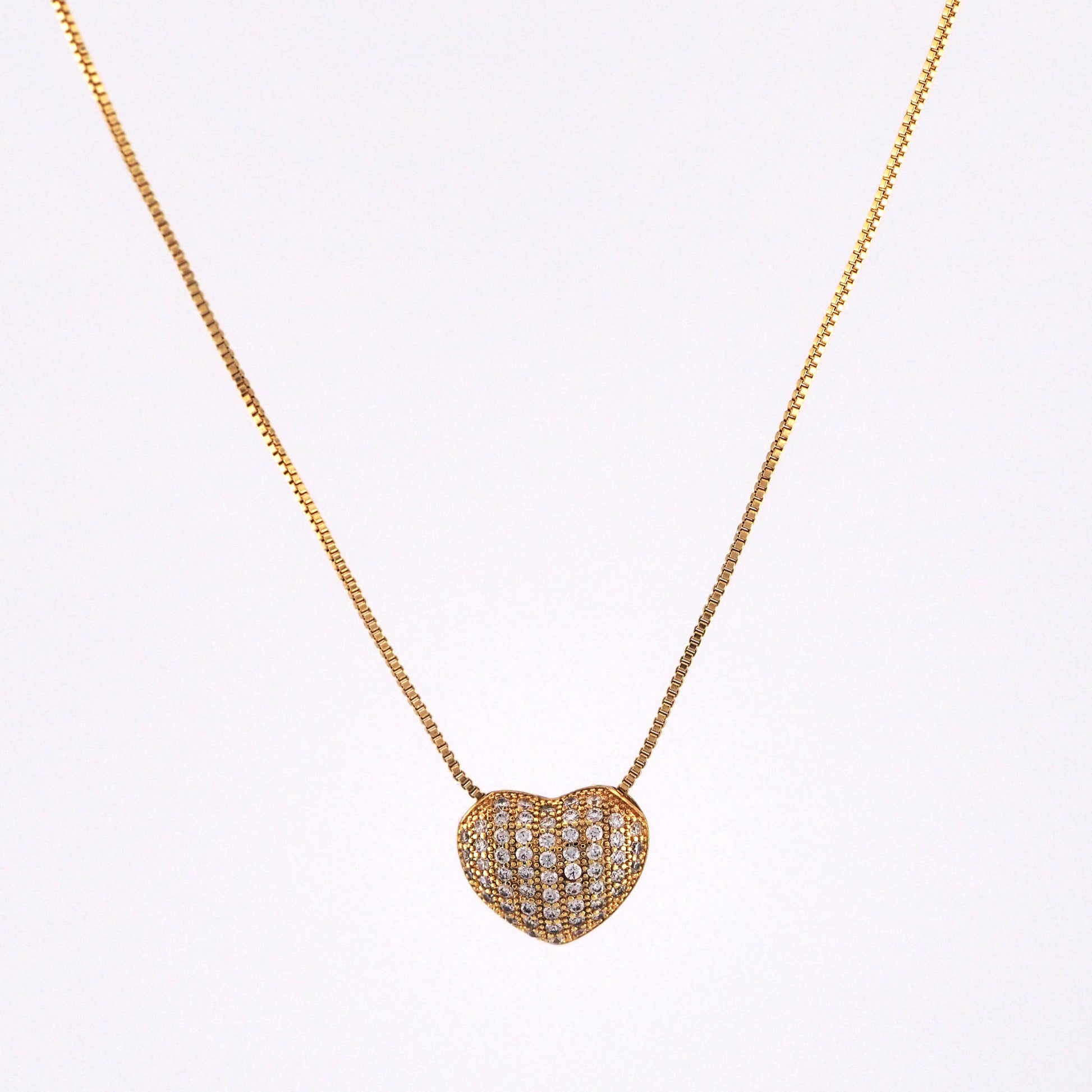 Heart-shaped diamond pendant on a gold chain against a white background