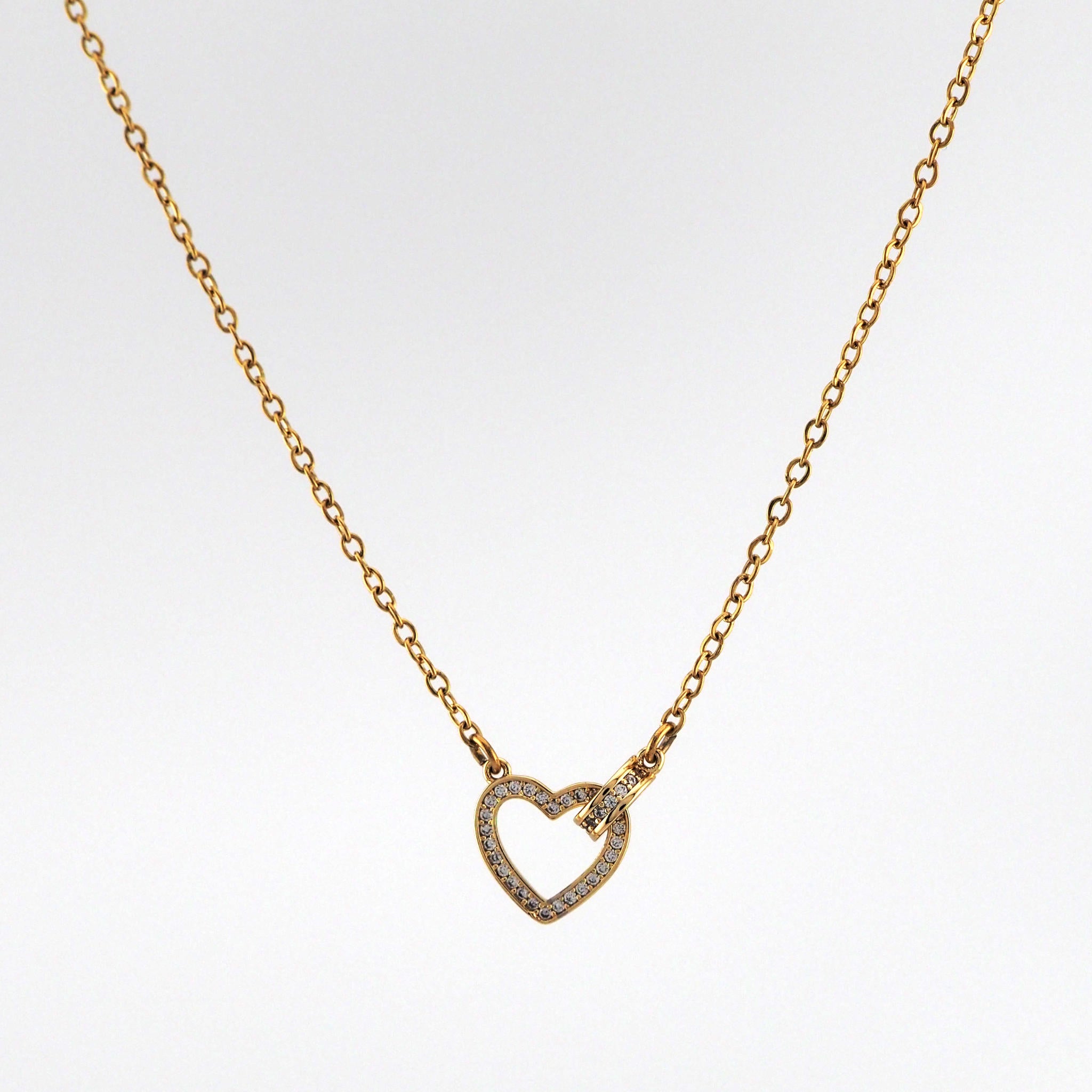 Gold necklace with a heart-shaped pendant on a light gray background