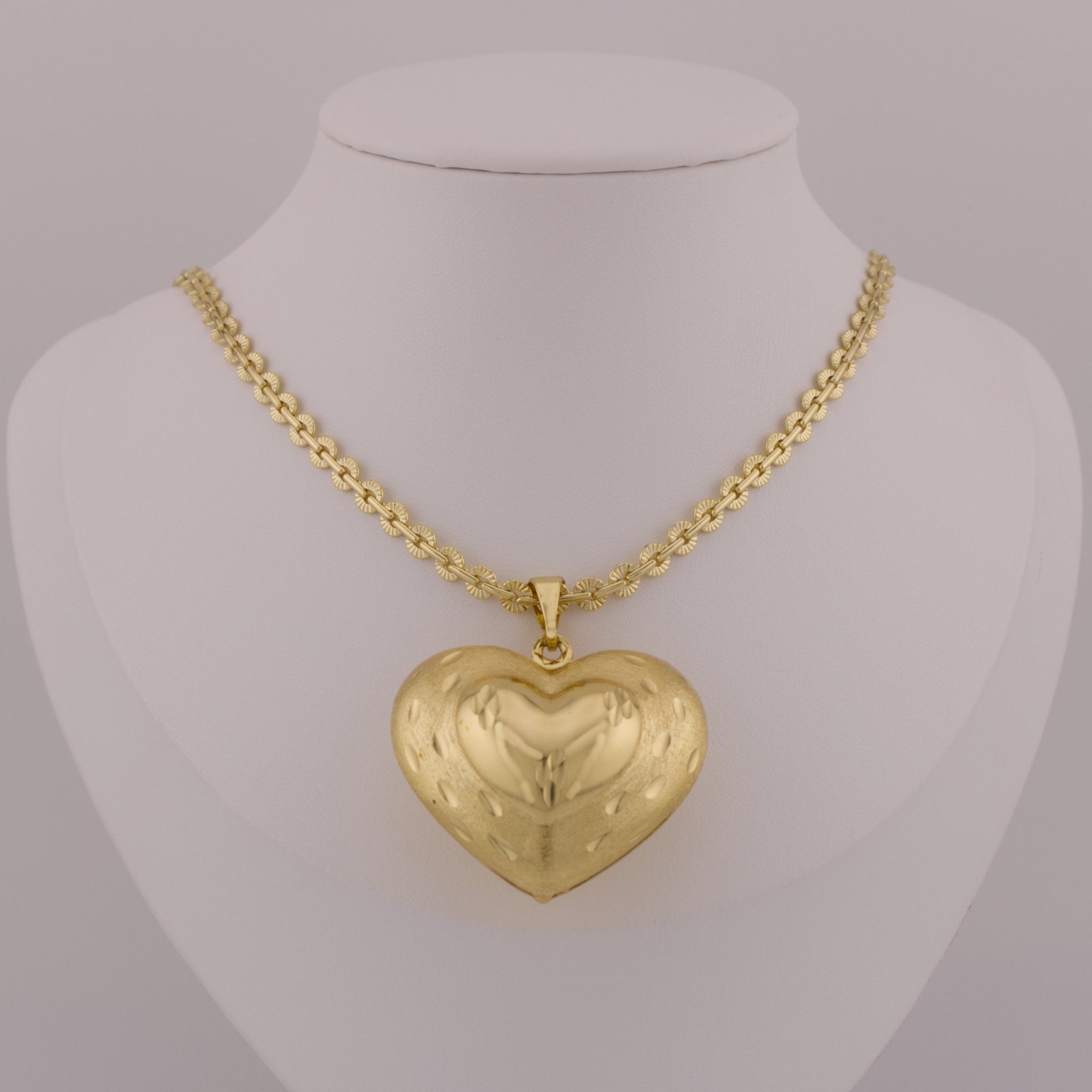 Gold heart-shaped pendant on a mannequin neck with a gray background