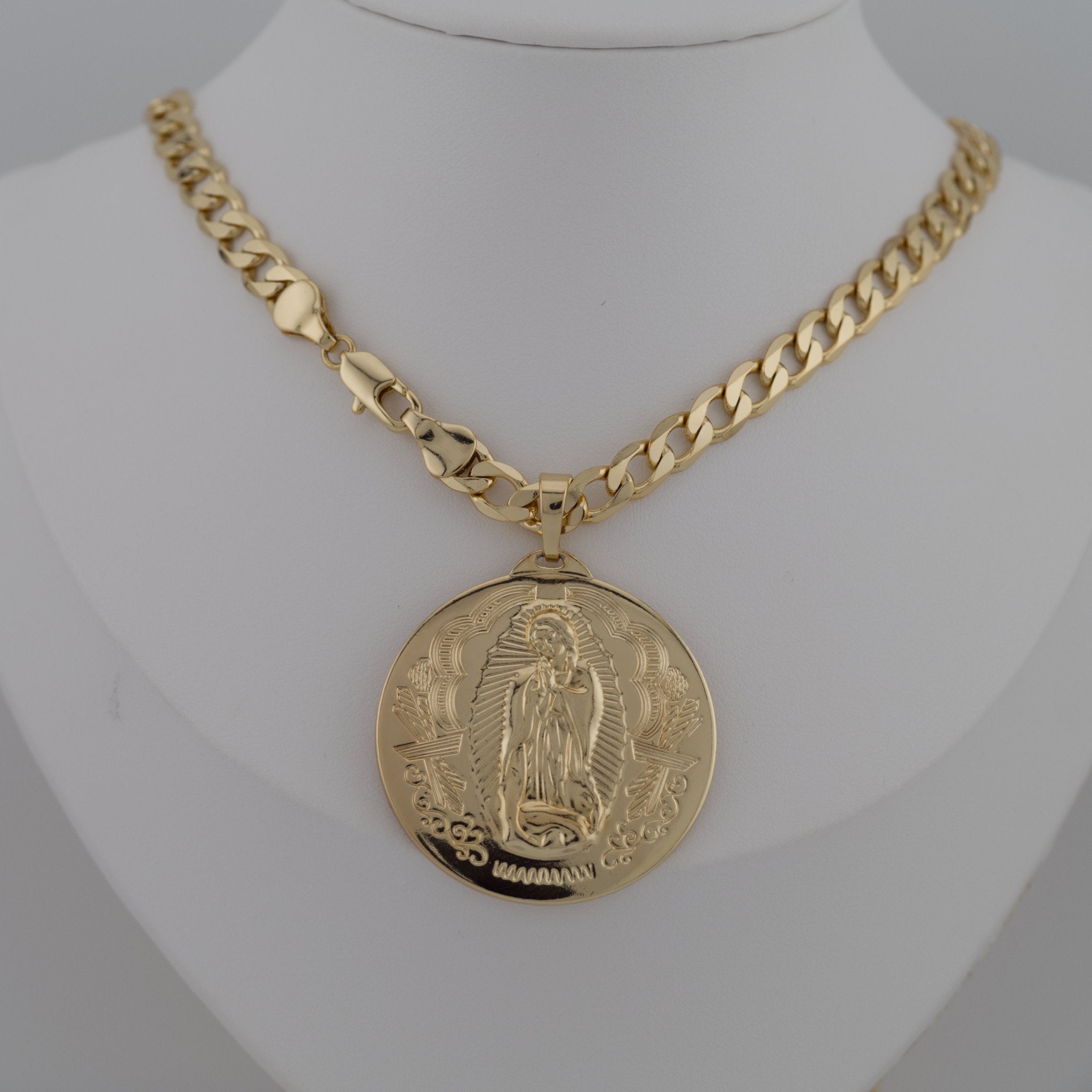 Gold chain necklace with a pendant on Virgen de Guadalupe against a gray background