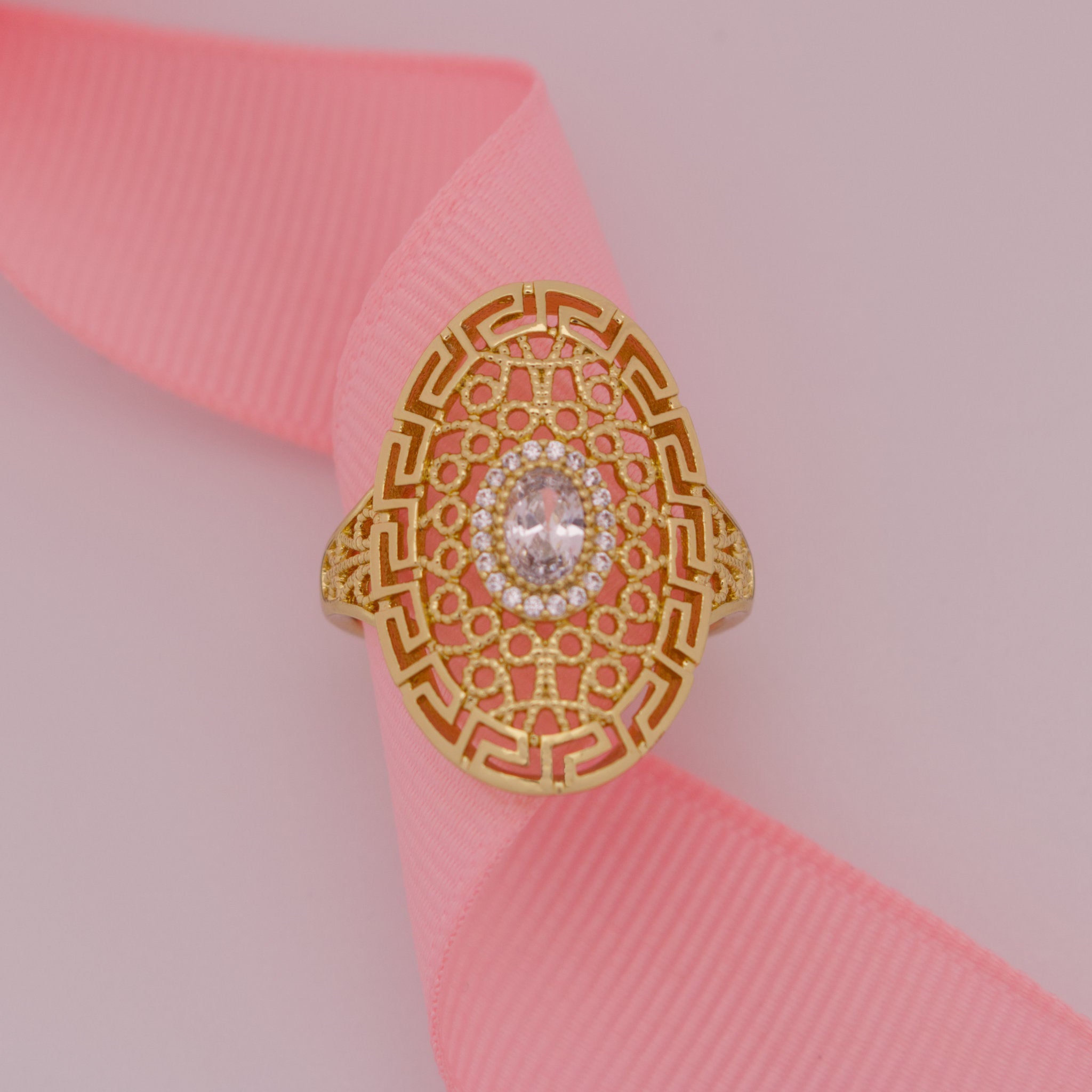 Gold ring with intricate design on a pink ribbon