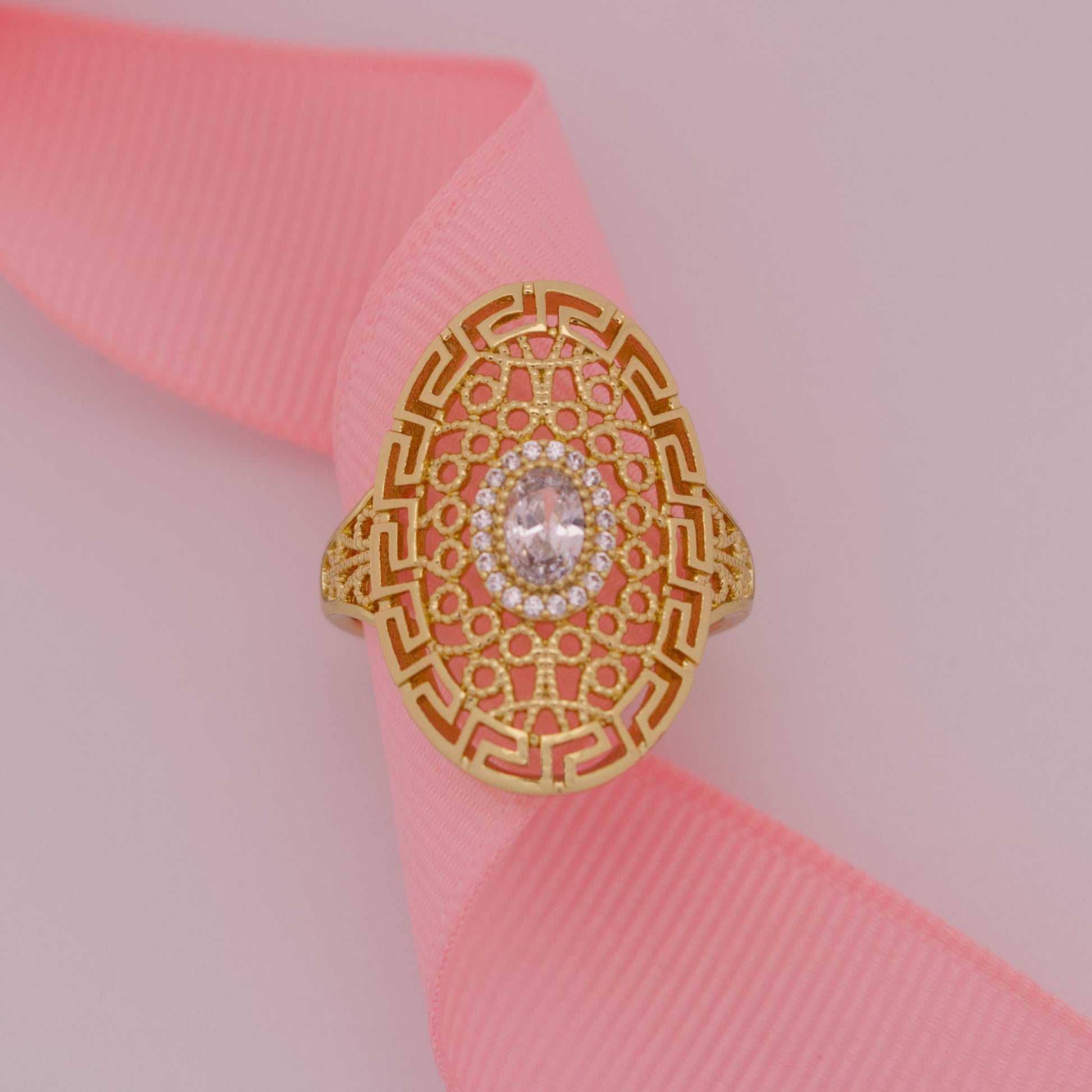 Gold ring with intricate design on a pink ribbon