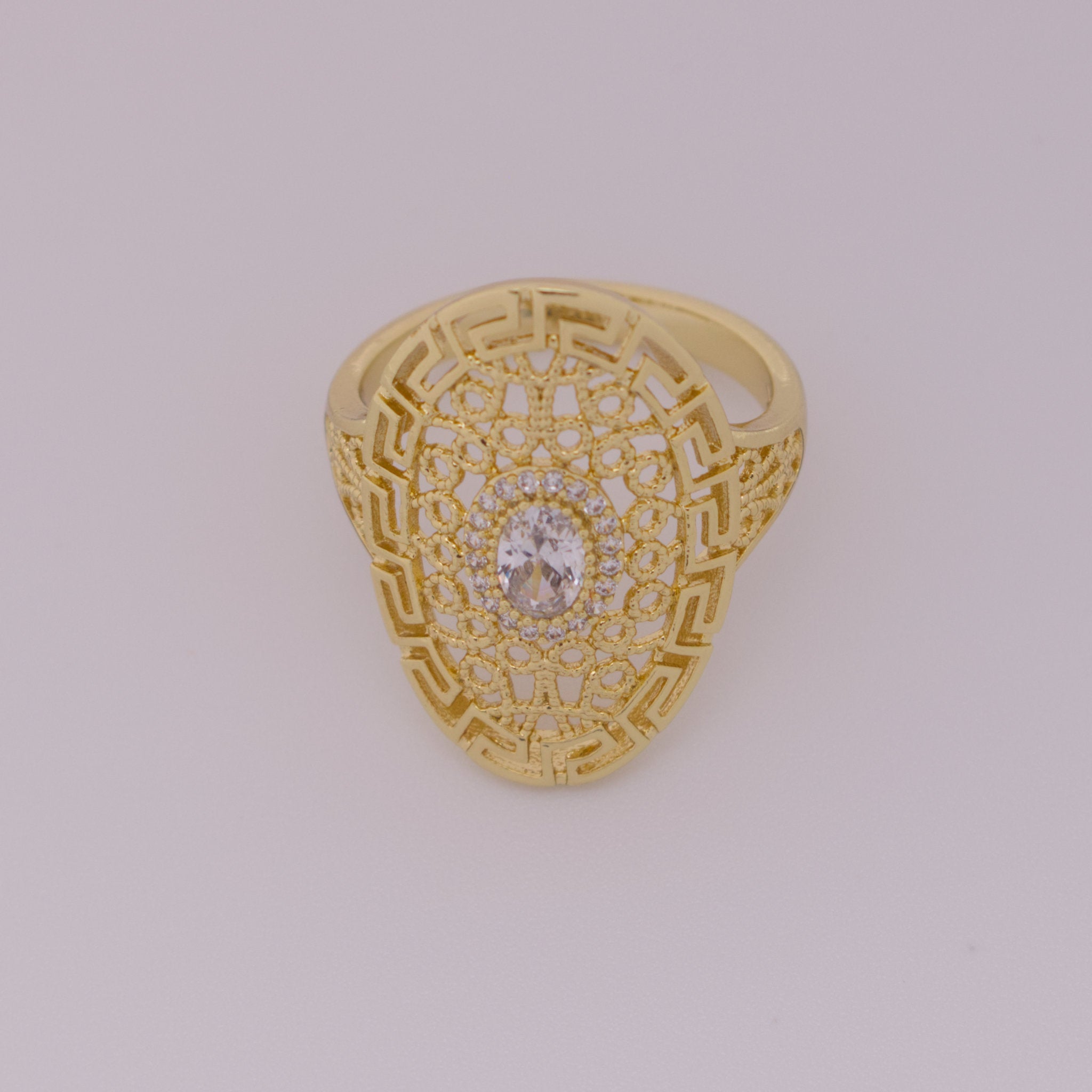Gold ring with intricate design and central gemstone on a light gray background