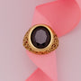 Gold ring with a dark gemstone on a pink ribbon